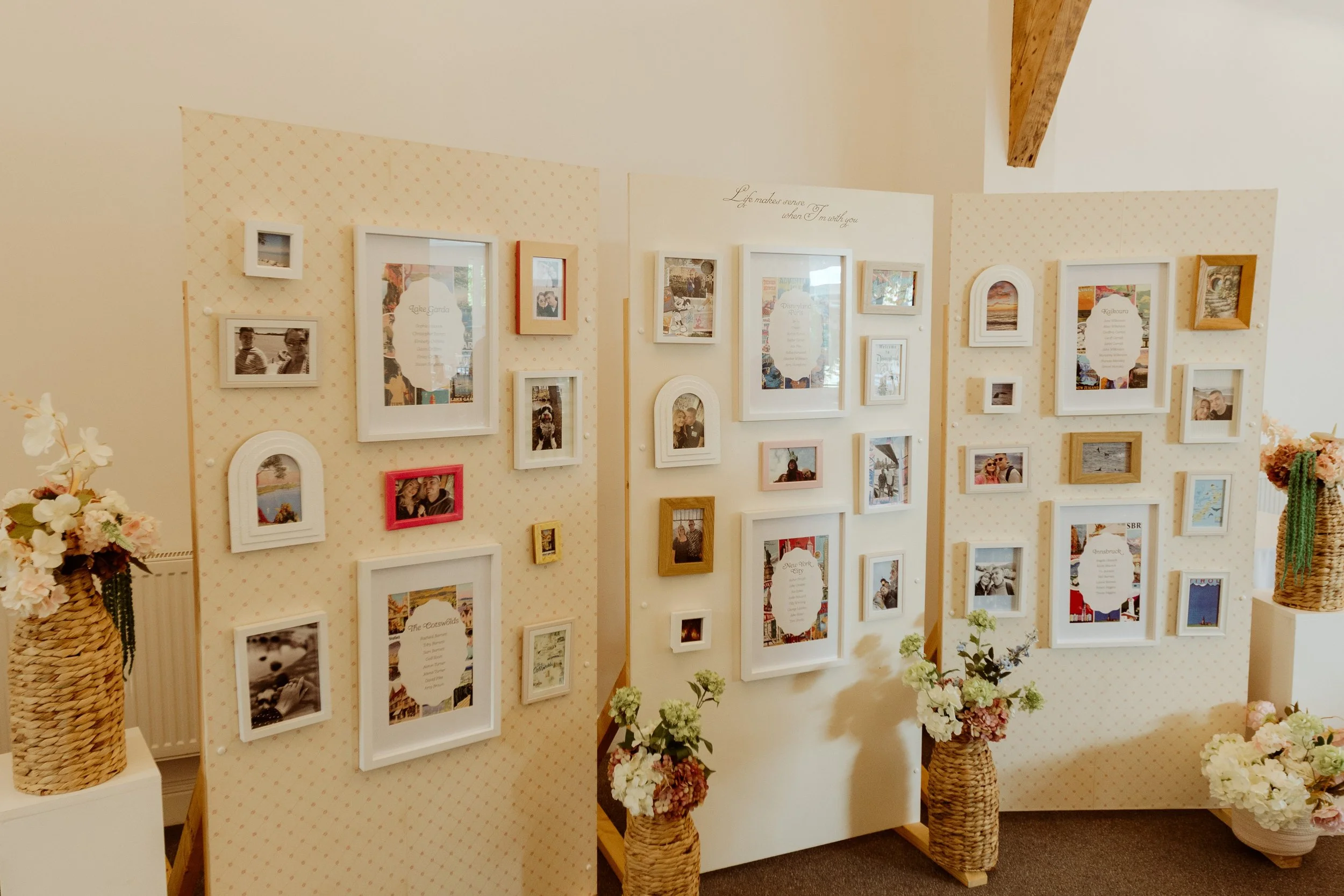 A photo display of framed photographs and art on a dotted light-colored background, with flowers in baskets at the base, in a cozy indoor setting.