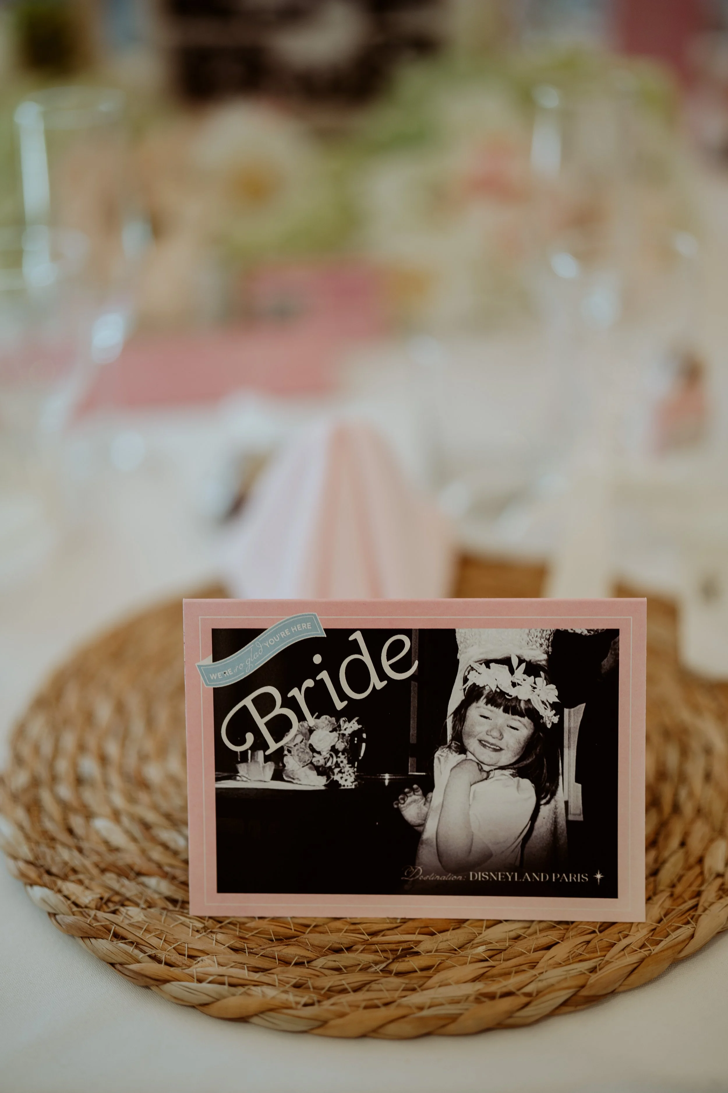 A pink wedding program or invitation with a black and white photo of a young girl laughing, inside a woven basket on a table.