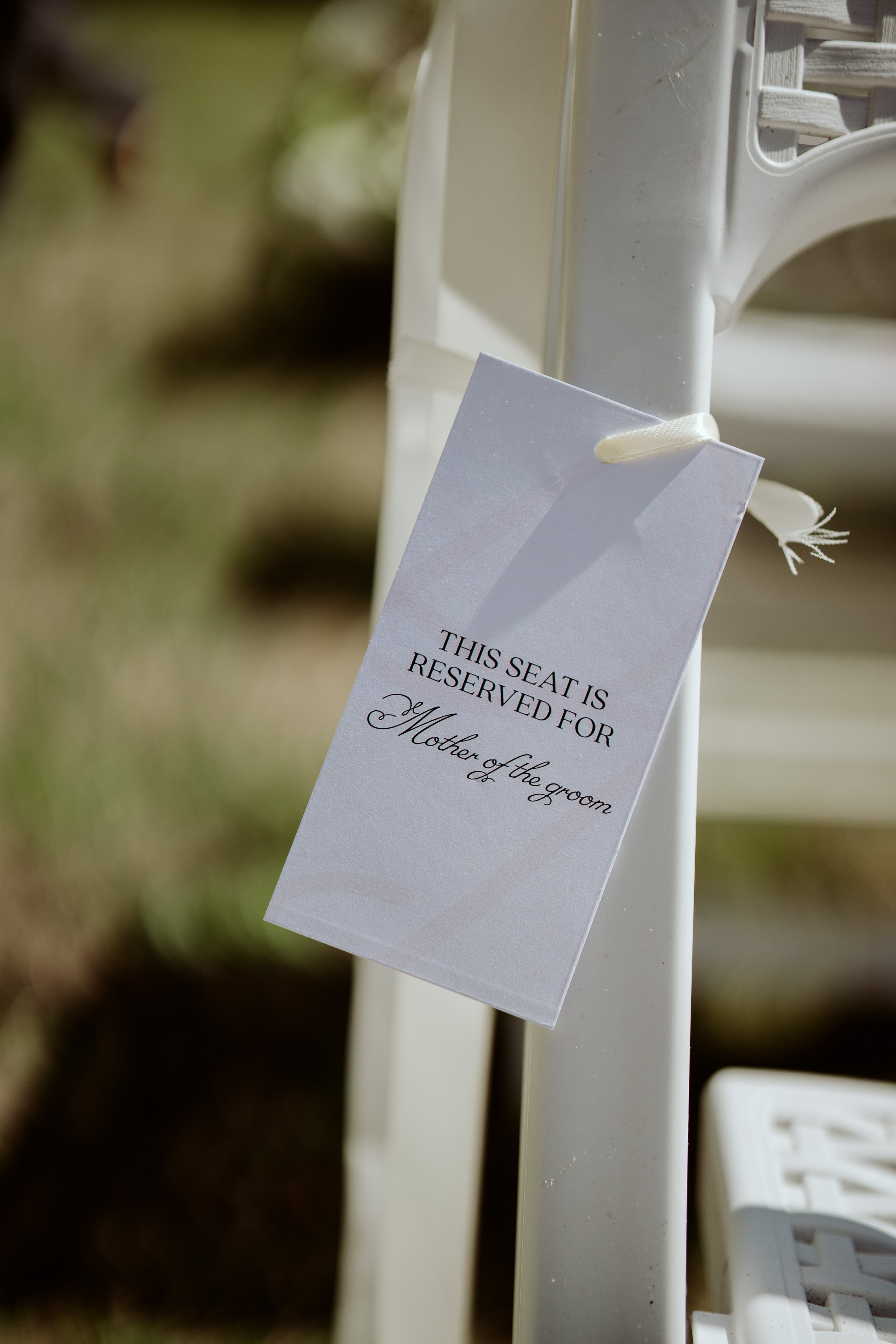 A reserved sign hanging on a white chair at a wedding reception, indicating the seat is reserved for the mother of the groom.