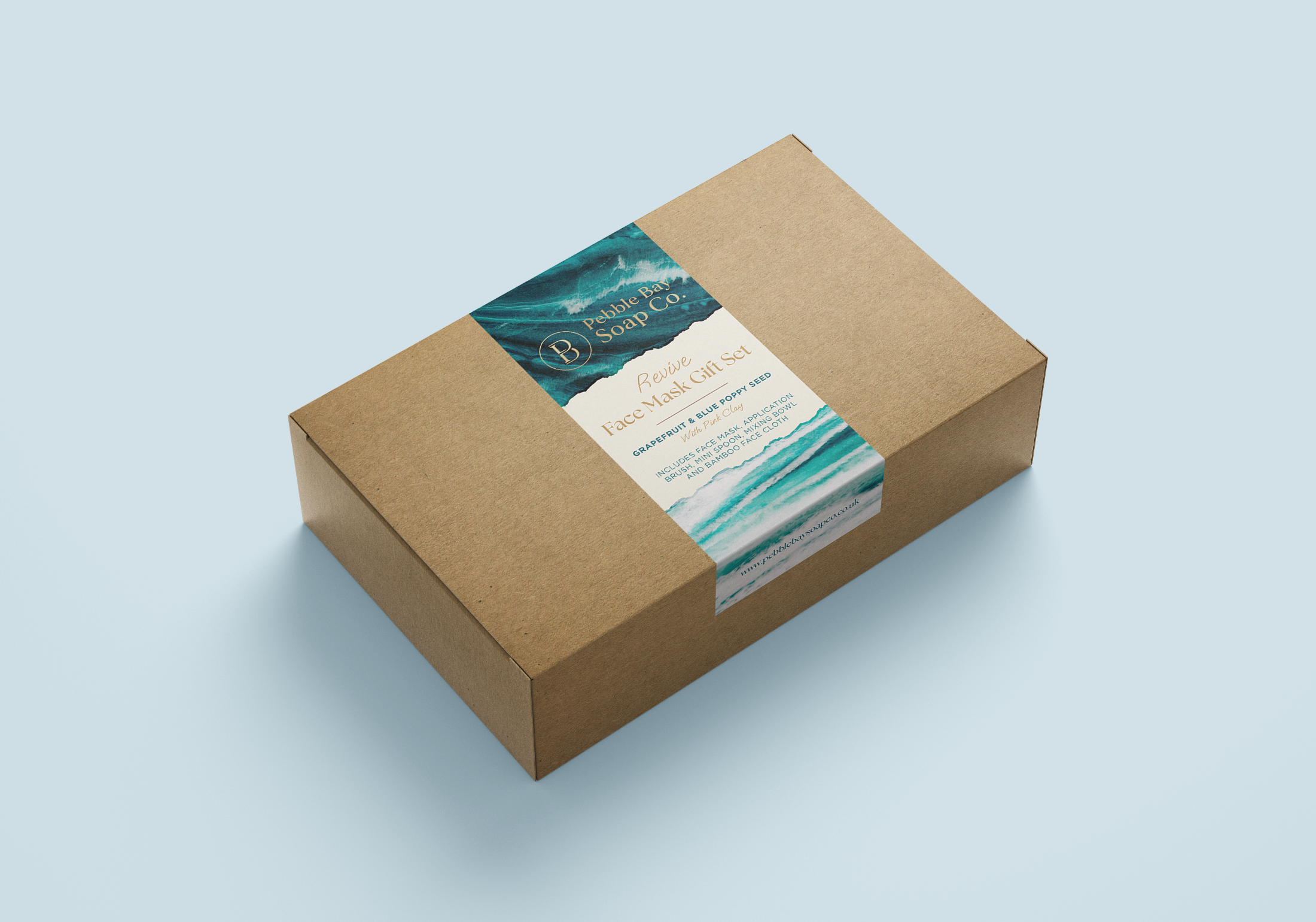 A cardboard box containing a set of soap called Pebble Bay Soap Co., with a label featuring ocean waves and text about ingredients and application.