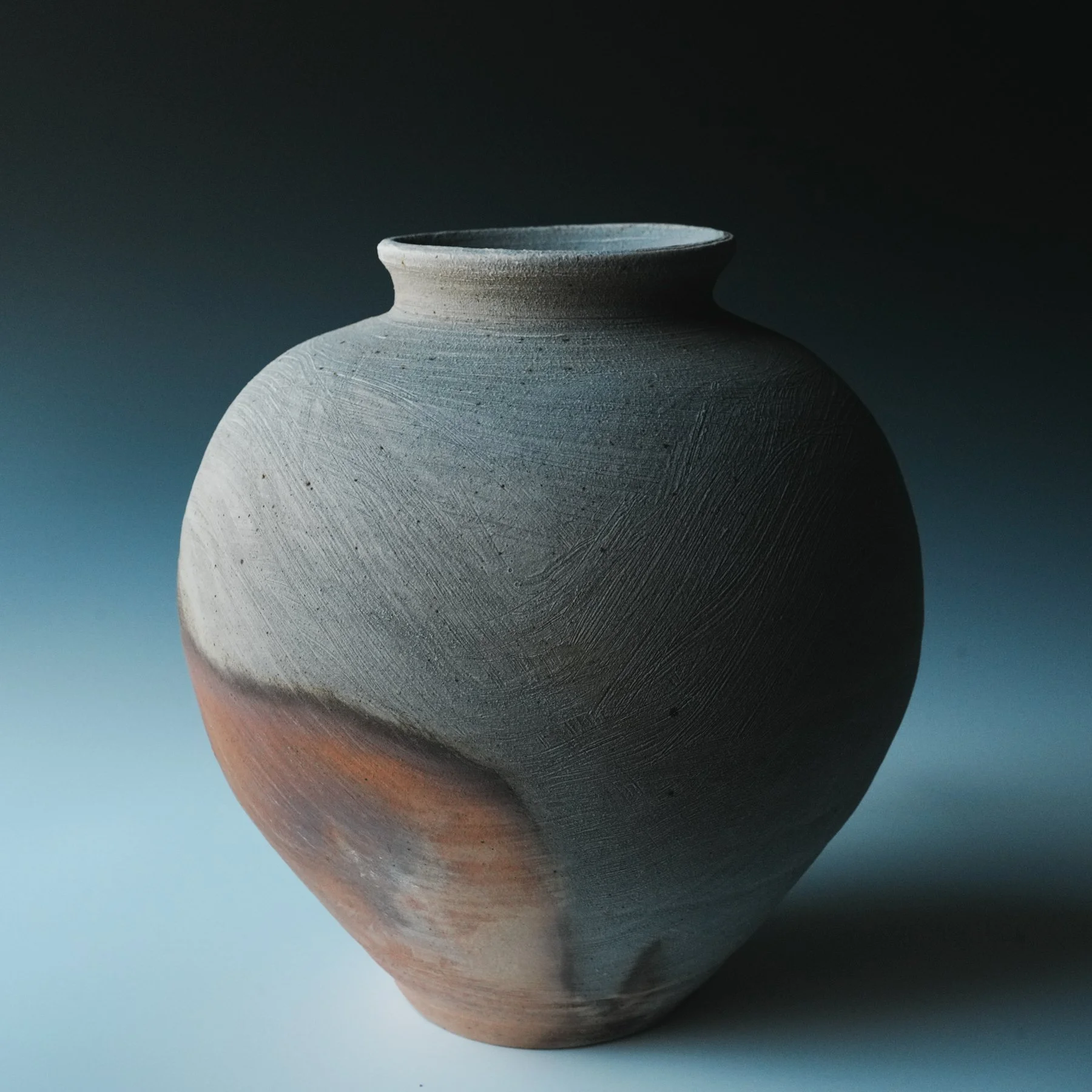 Close-up of a gray ceramic vase with a rounded body and a narrow neck, placed against a dark background.