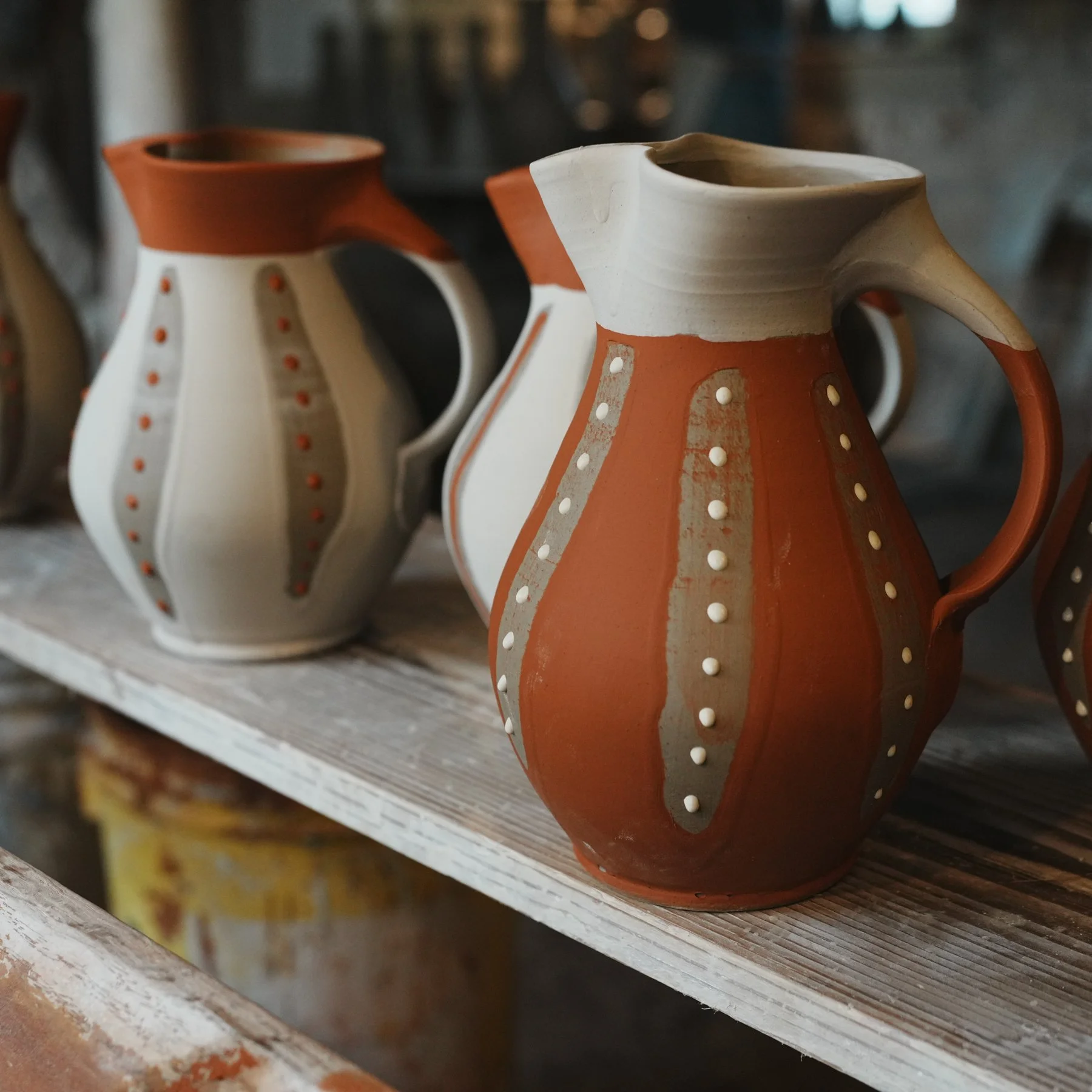 Close-up of three handcrafted pottery vases with geometric patterns, mainly in terracotta and cream colors, displayed on a rustic wooden shelf.
