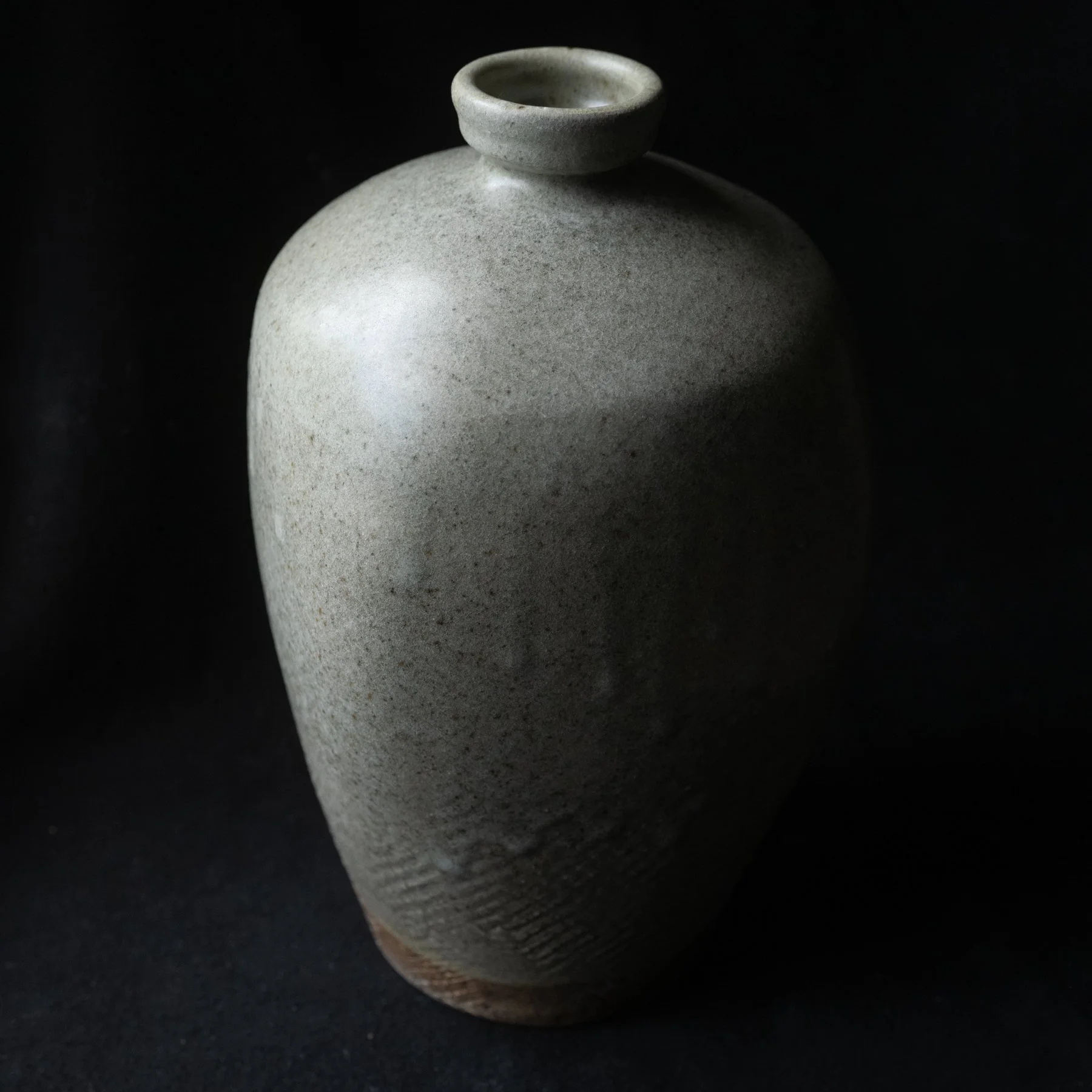 A gray ceramic vase with a narrow neck and a rounded body, set against a black background.