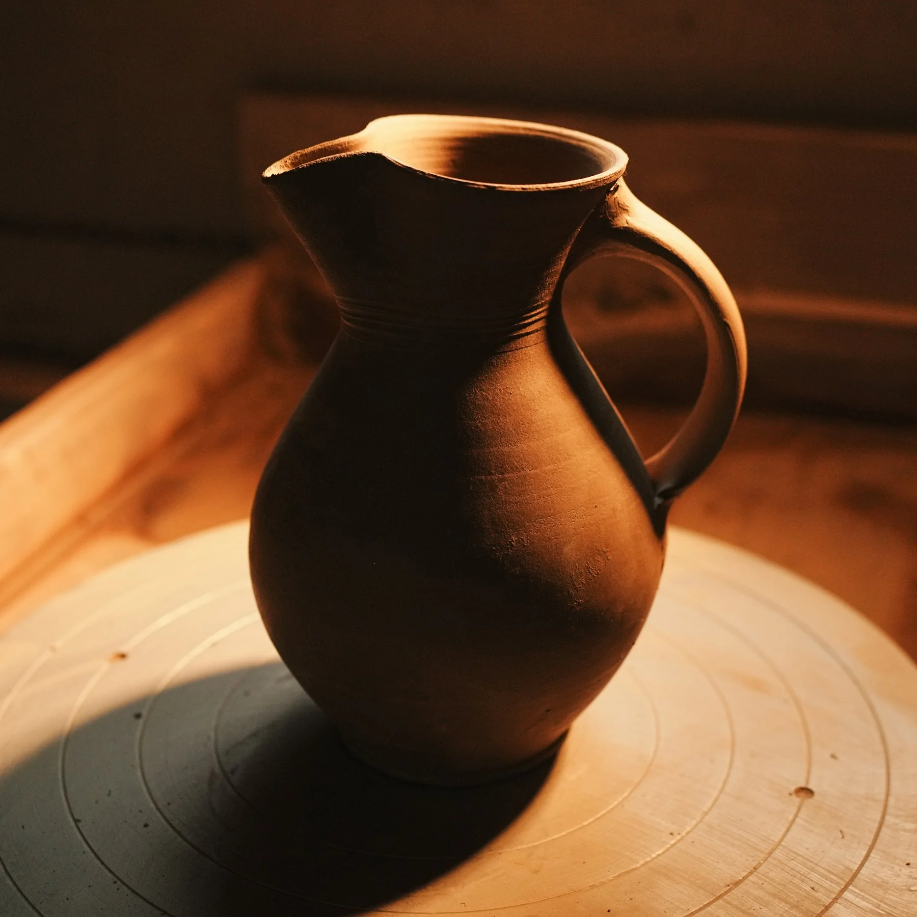 Close-up of a clay pottery vessel on a potter's wheel, illuminated by warm light.