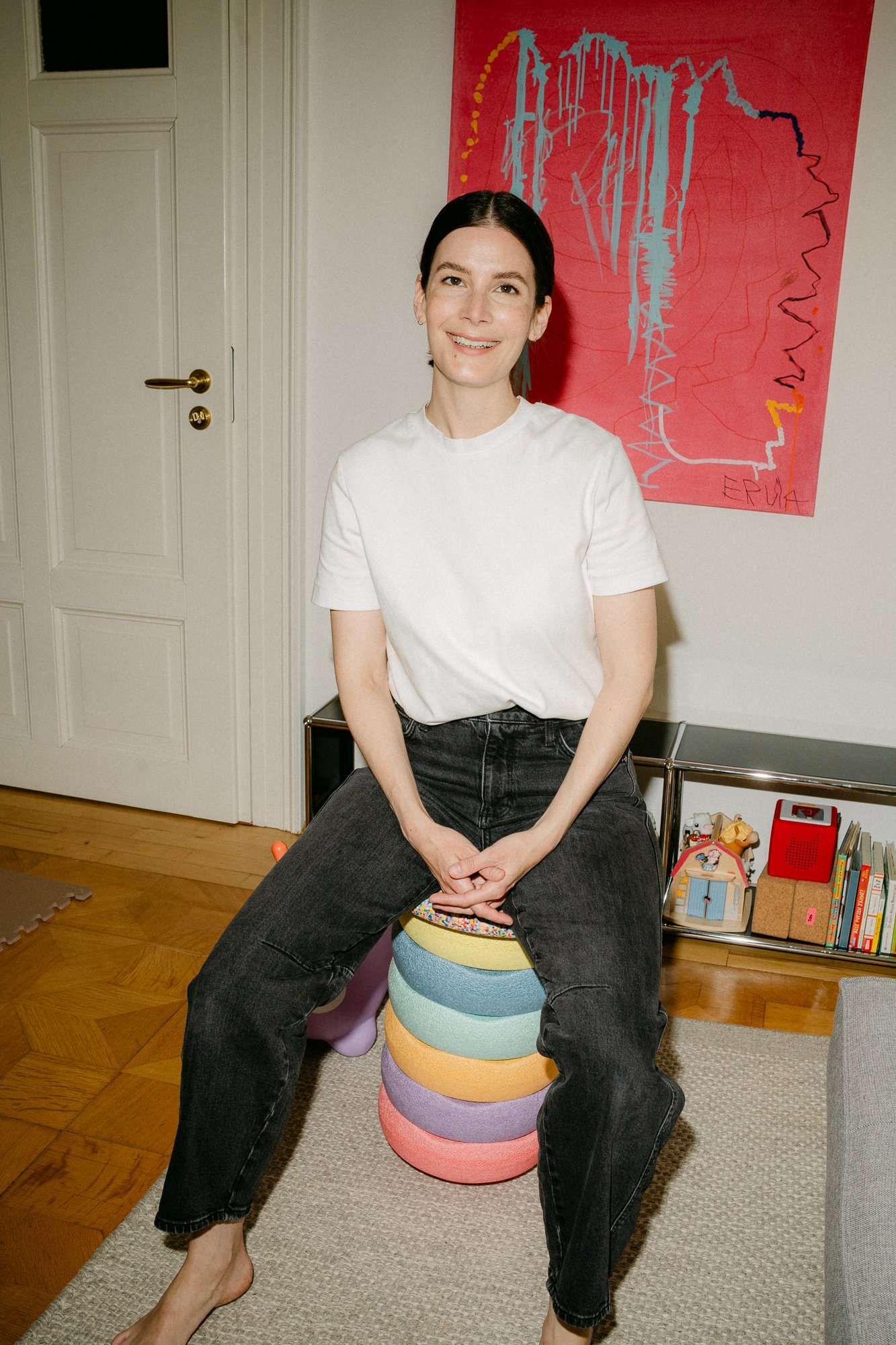 Woman in white t-shirt sitting on stacking toy beside pink artwork — editorial brand photography Leipzig