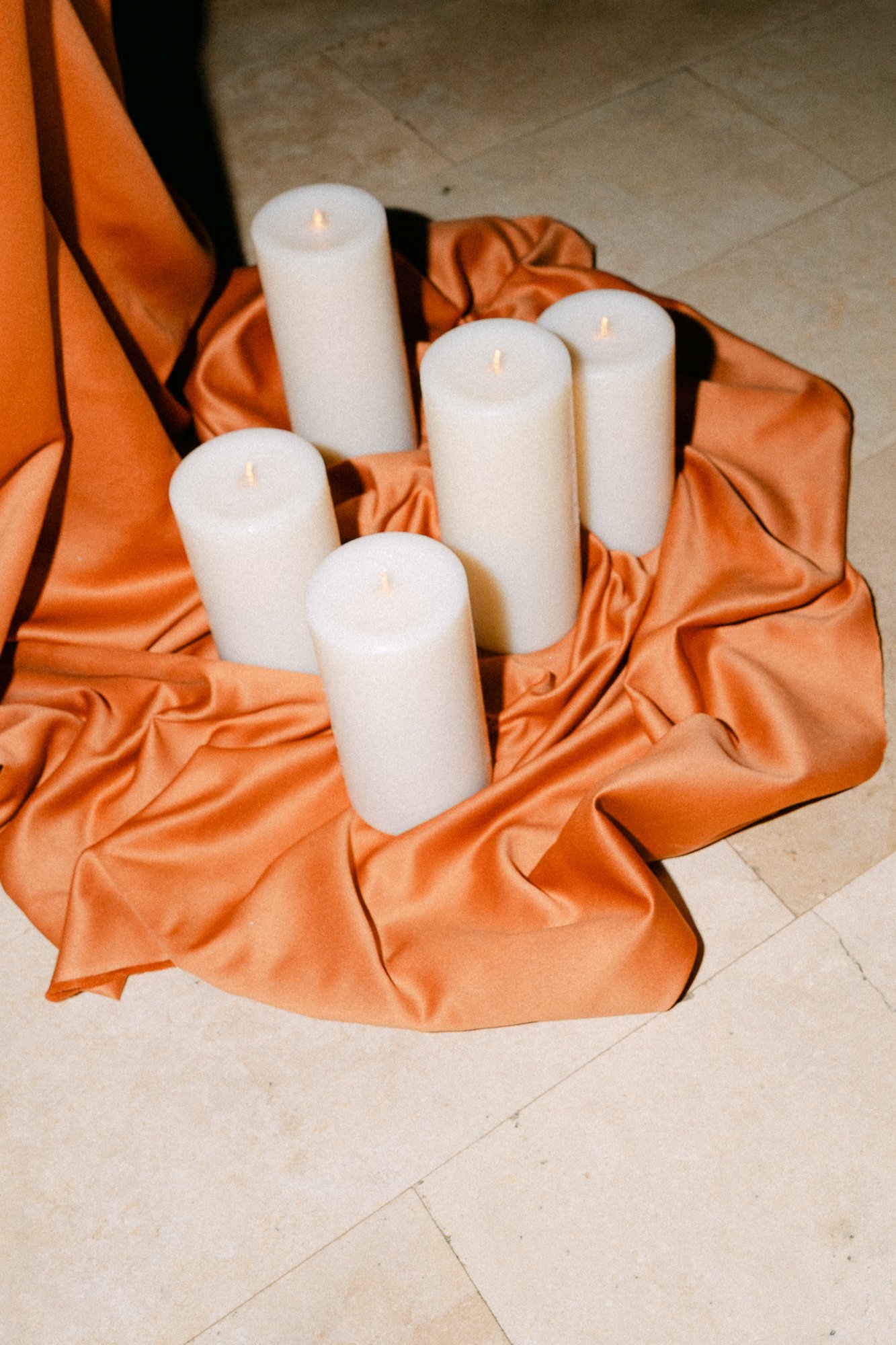White candles arranged on burnt orange fabric — wedding detail photography Tuscany