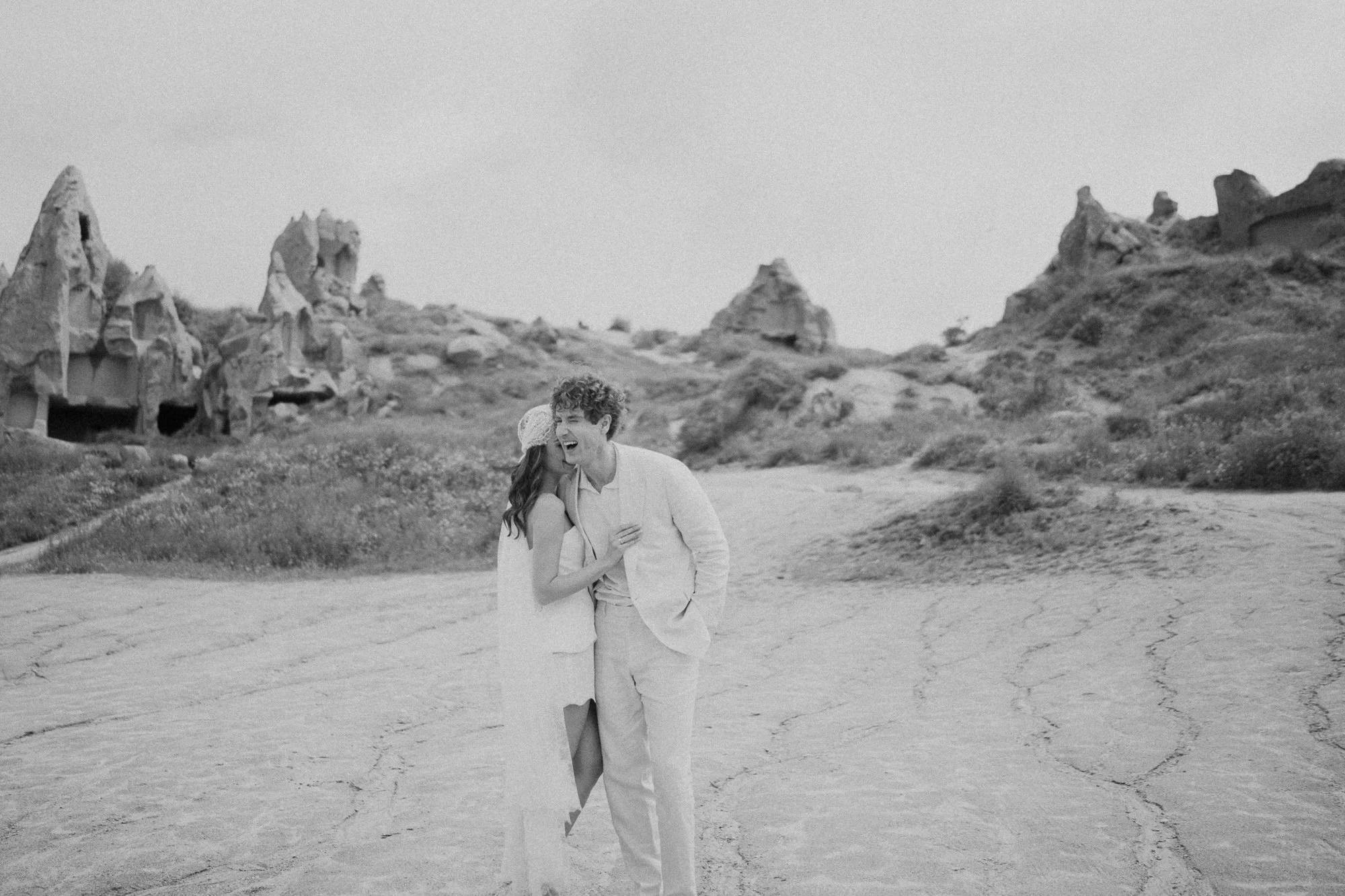 Bride and groom walking in wide Cappadocia landscape with horses in background