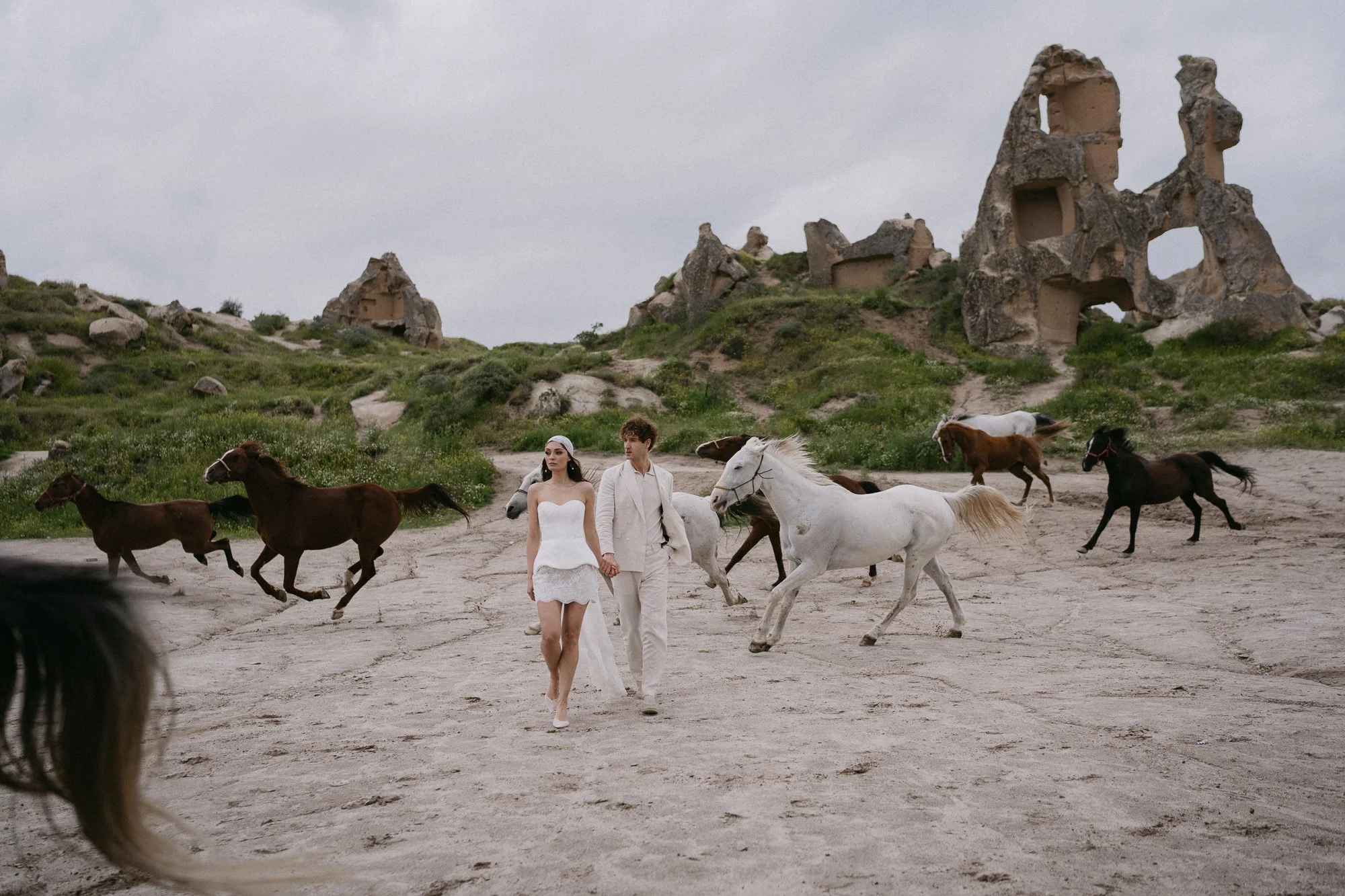 Bride and groom walking in wide Cappadocia landscape with horses in background