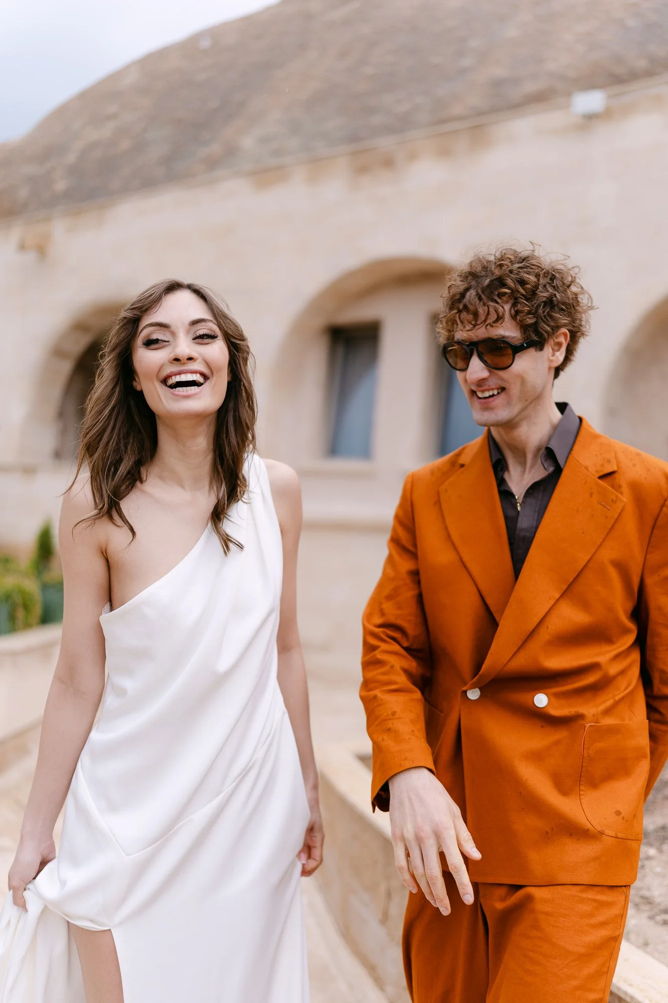Man in rust-orange suit and woman in white dress on Tuscany terrace — destination wedding editorial photography