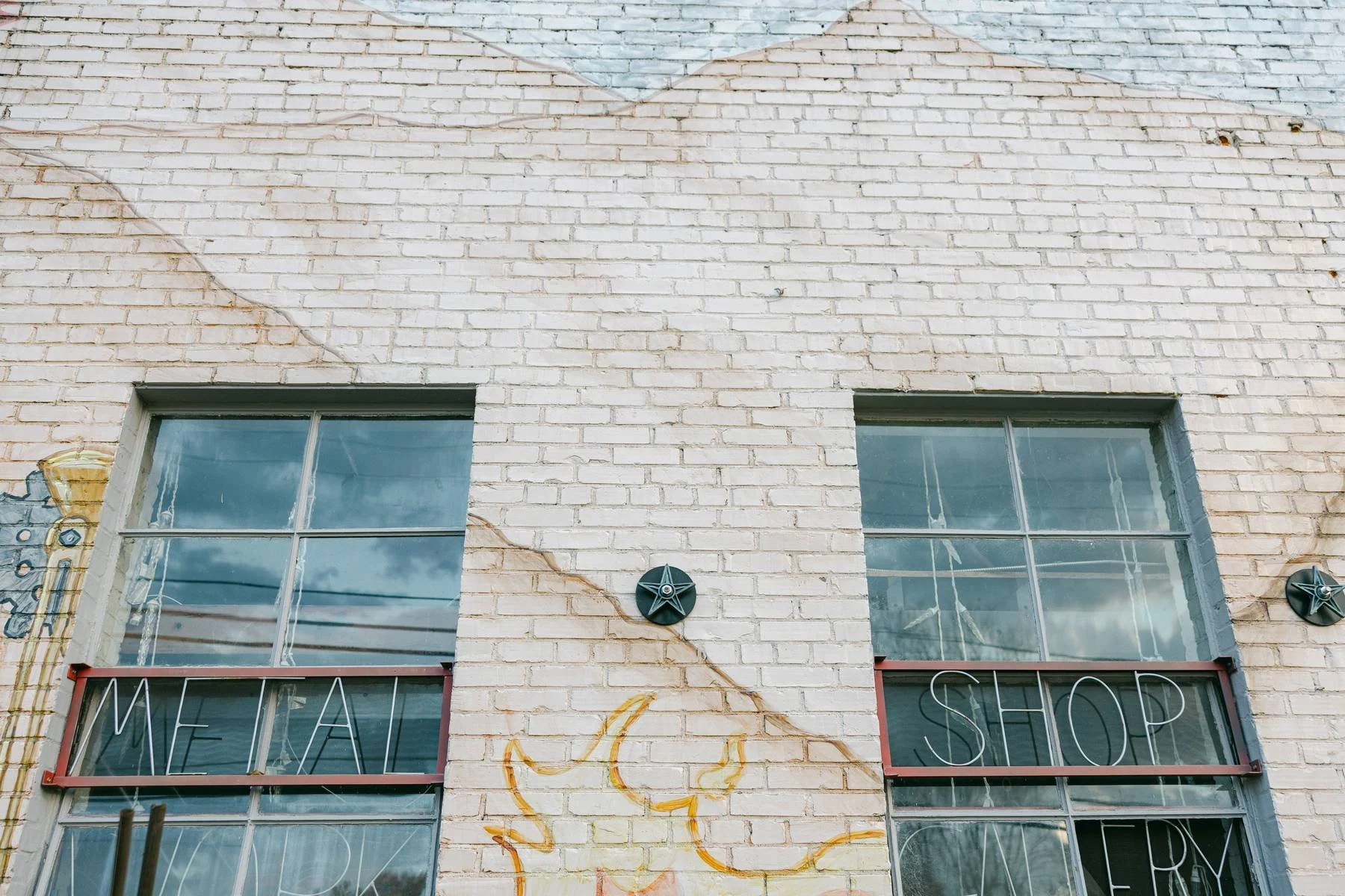 White brick building with two large windows and light bulb signs. A yellow moon drawing is on the brick wall below the windows.
