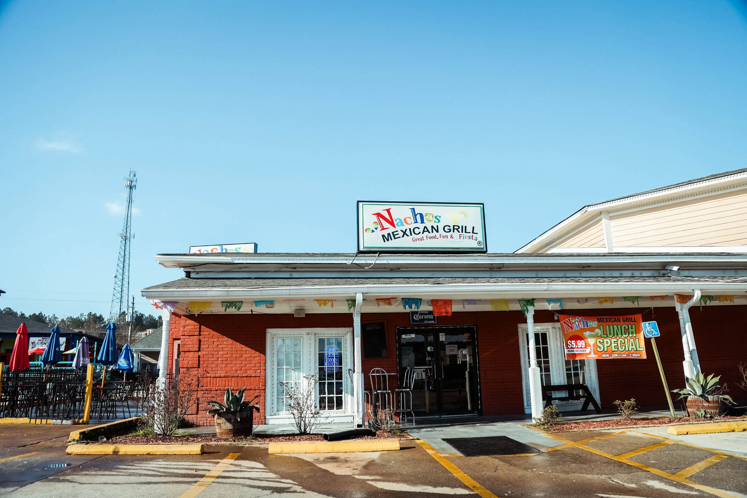 Exterior view of Nachos Mexican Grill, a restaurant with red brick walls, a sign on top, outdoor seating with umbrellas, and a banner advertising a lunch special for $5.99.
