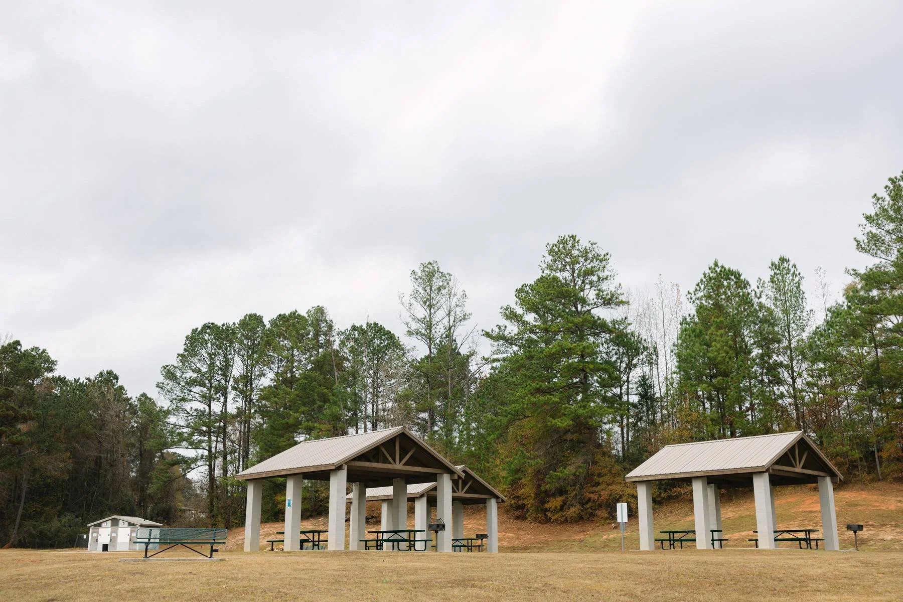 Park with two picnic shelters and a grassy area, surrounded by trees and an overcast sky.