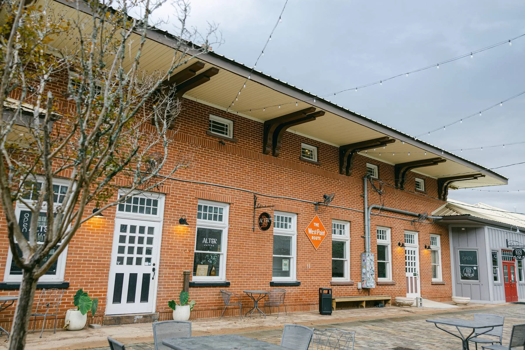 Brick building with outdoor seating, string lights, and a sign that reads 'The West Point Route'.