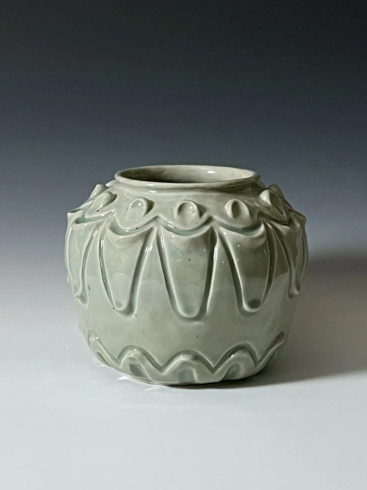 A light green ceramic vase with decorative drips and ridges around its top and bottom edges.