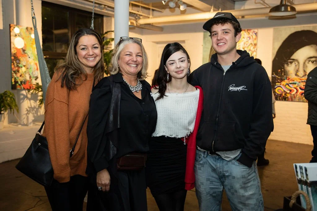 Group of four people smiling at an art gallery event with artworks in the background.