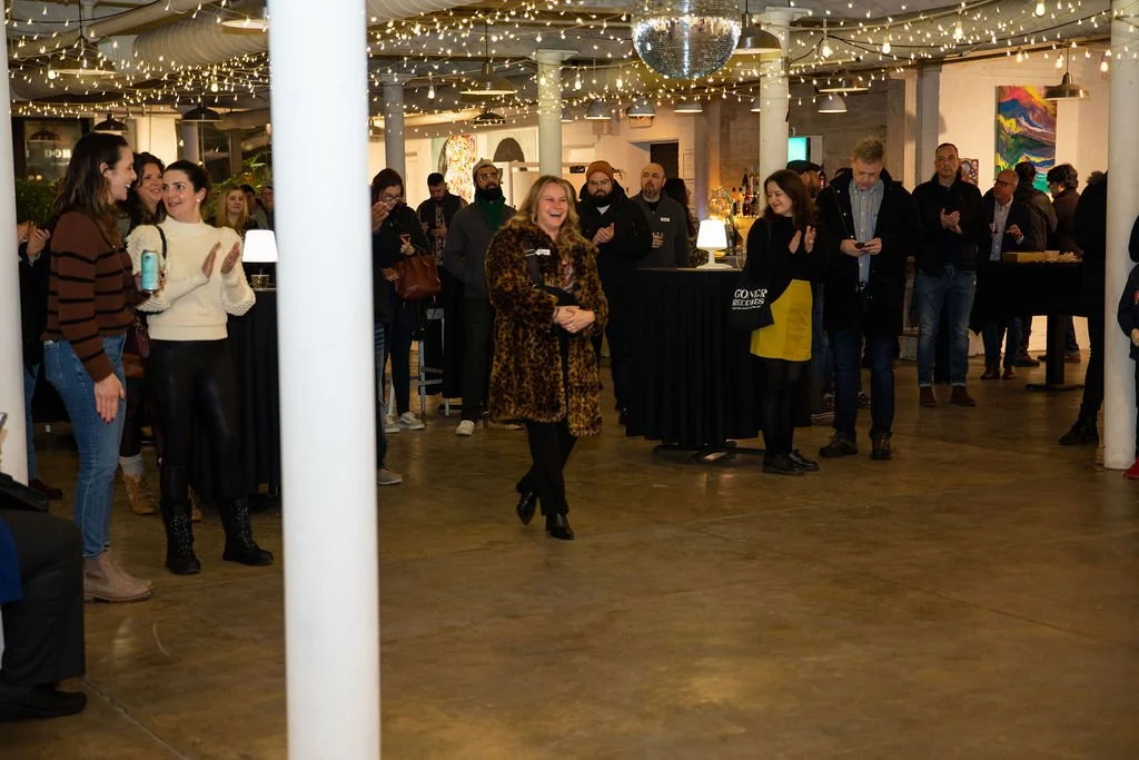 People gathered in a decorated indoor space, with string lights and a disco ball overhead, socializing and clapping.