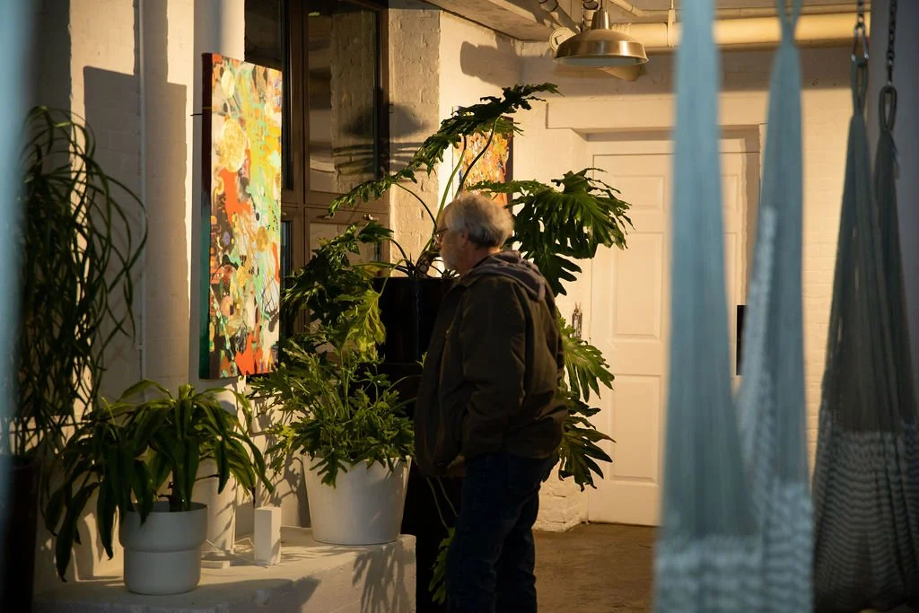 Person observing colorful art in a plant-filled gallery space