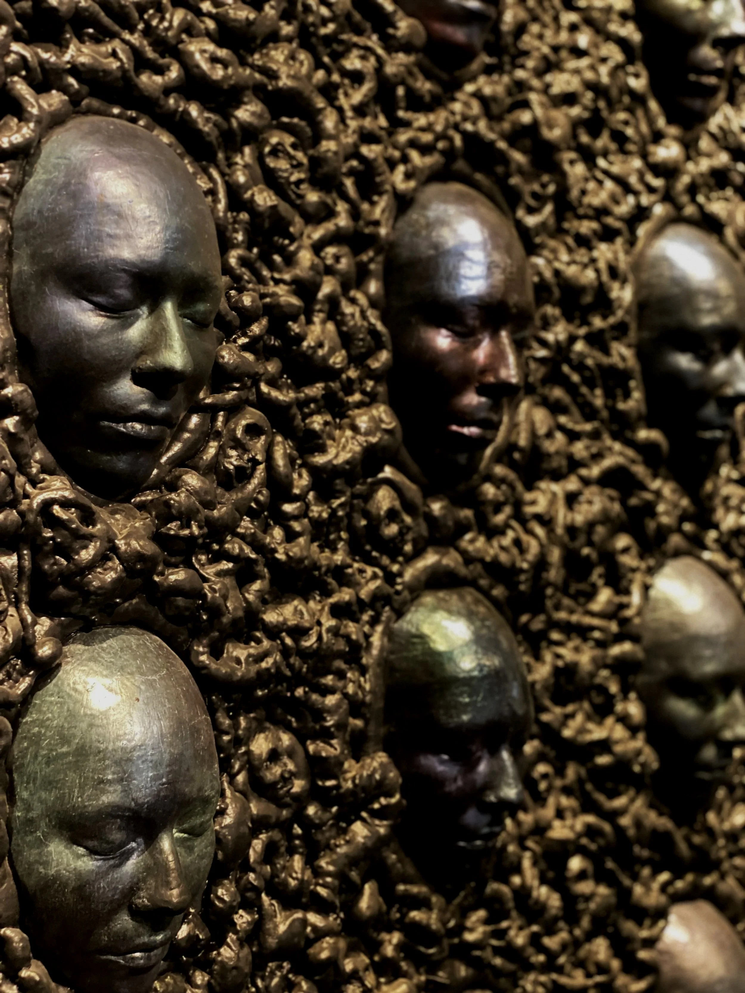 Arrangement of faces on a wall in black tar-like background