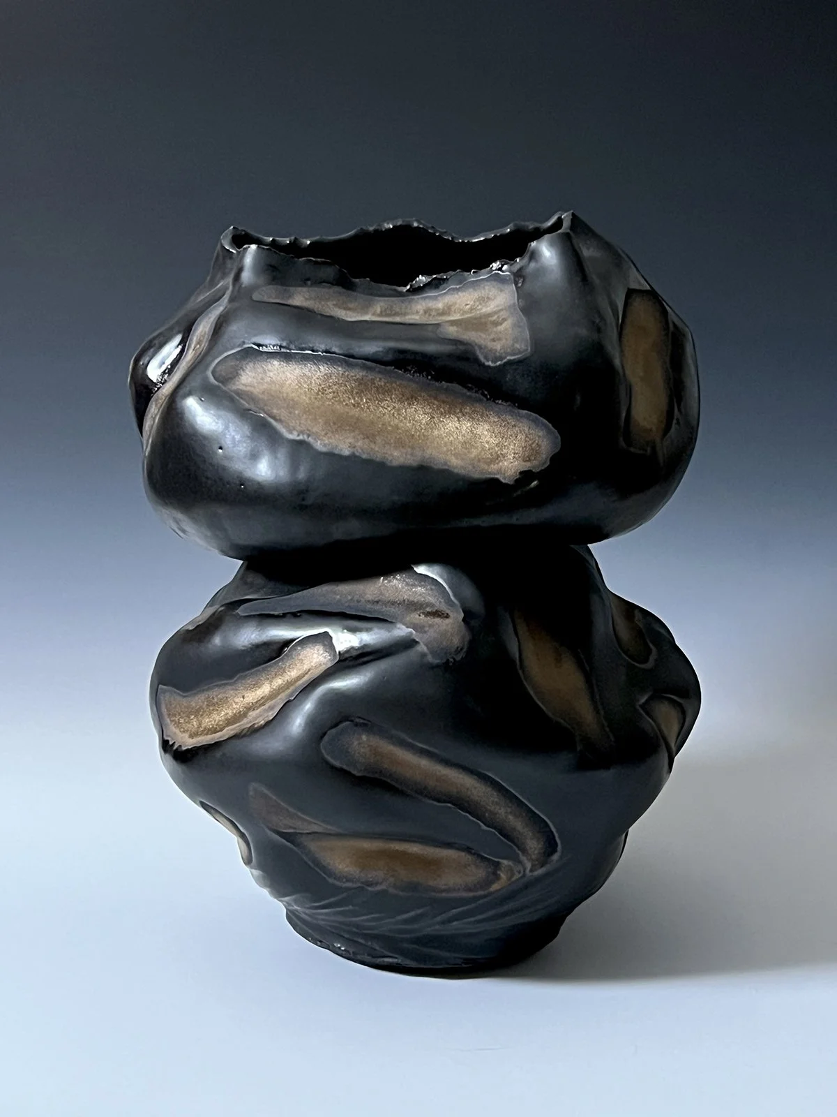 Two black and gold marbled glass vases stacked together against a gradient background.