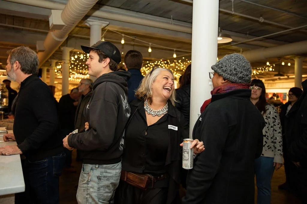 People socializing at an indoor event with festive lights, featuring a smiling woman in conversation, holding a drink.