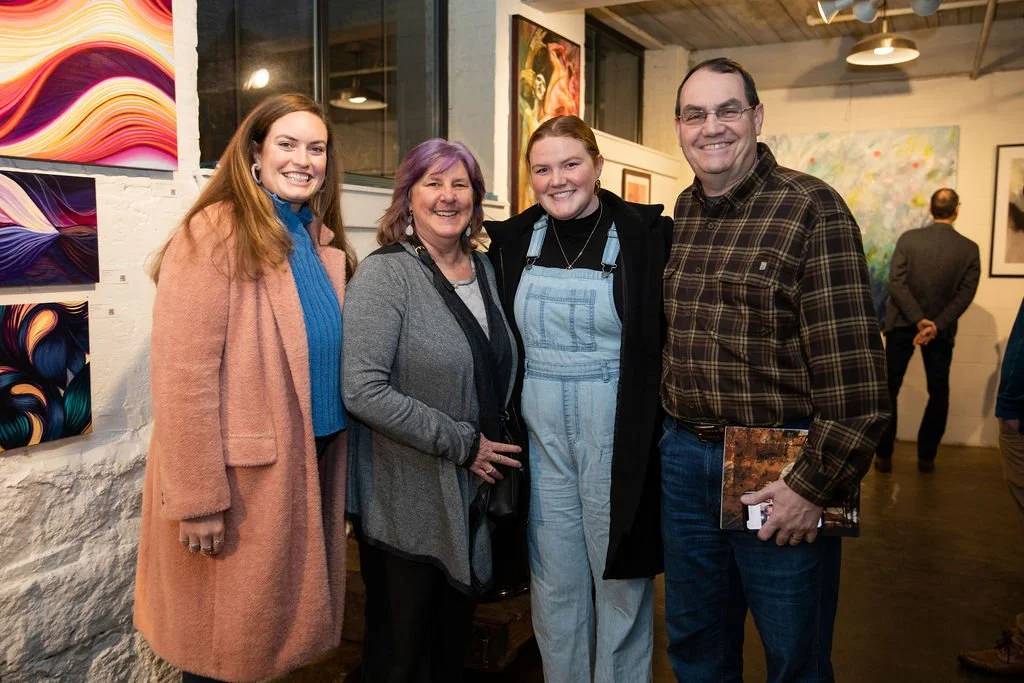 Four people in a gallery setting, standing in front of abstract art pieces on the wall.