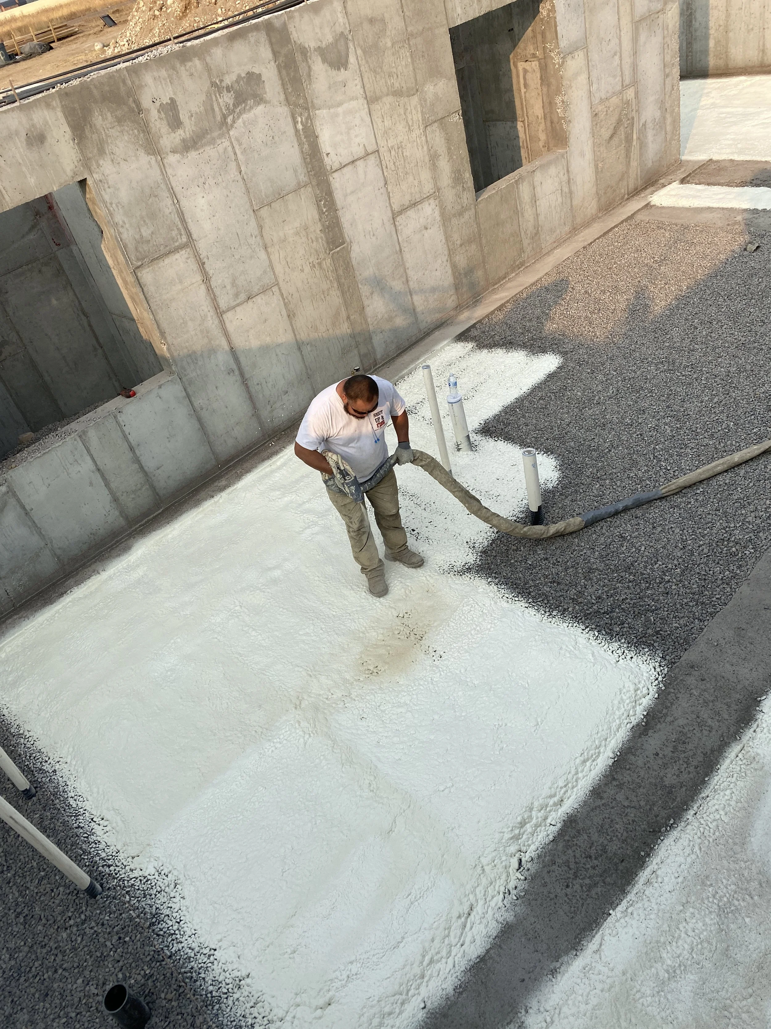 Construction worker spraying a foam insulation on the ground at a building site.