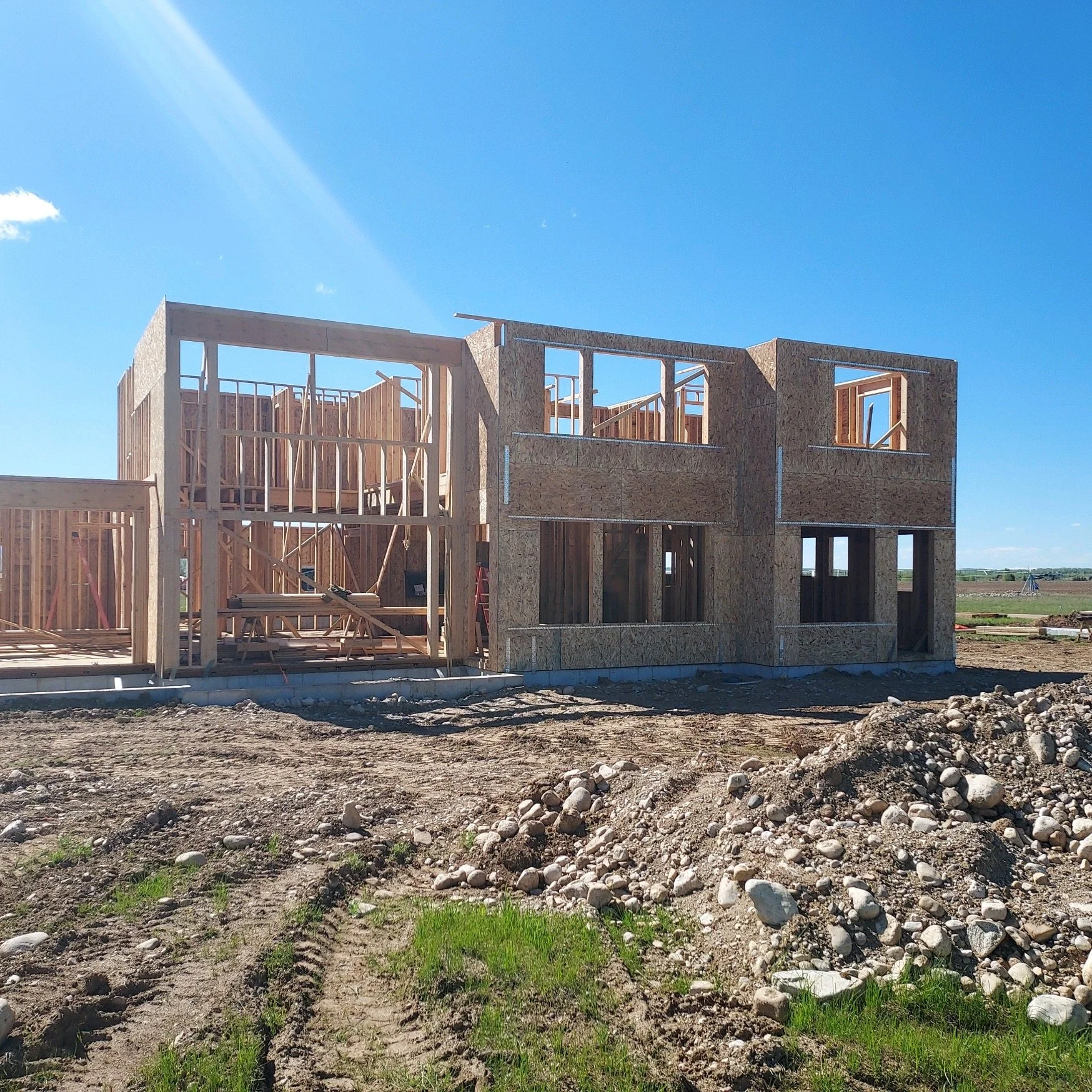 Wood frame house under construction with blue sky and open land in the background.