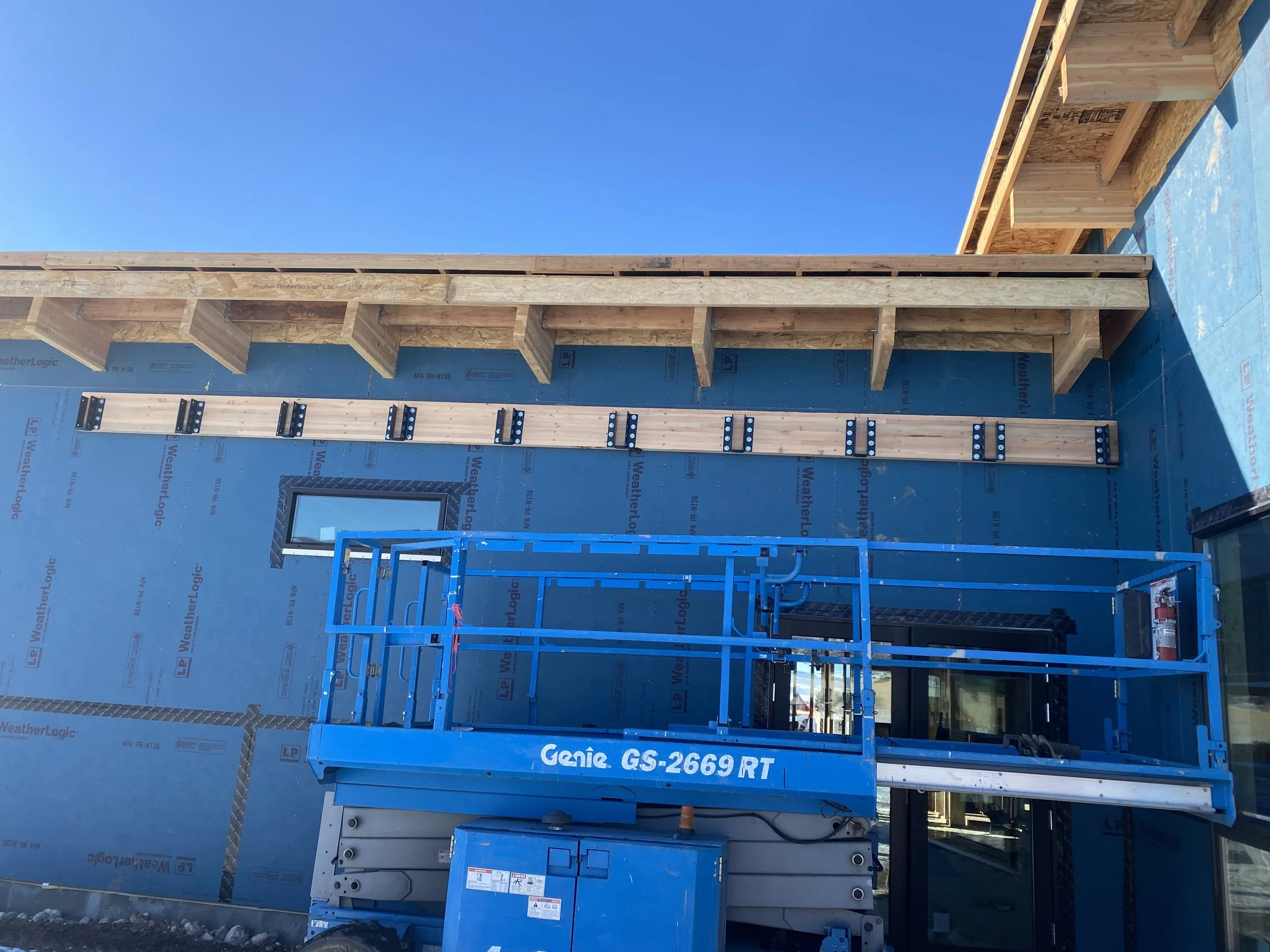 Construction site with a blue Genie lift and wooden framework on a partly built building, under a clear blue sky.