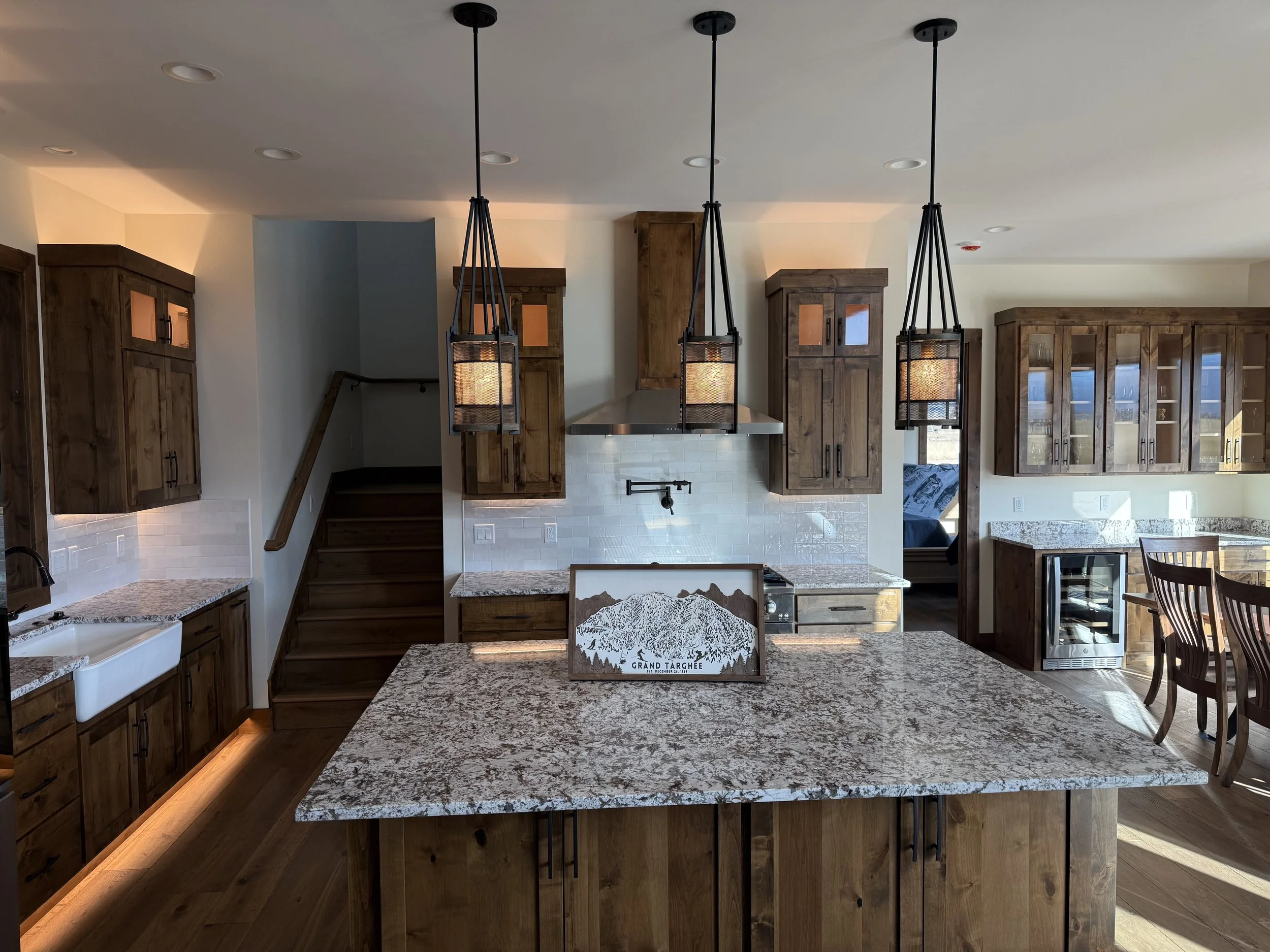 Custom kitchen with granite countertops, wood cabinetry, large island, and pendant lighting in a  Driggs custom home.
