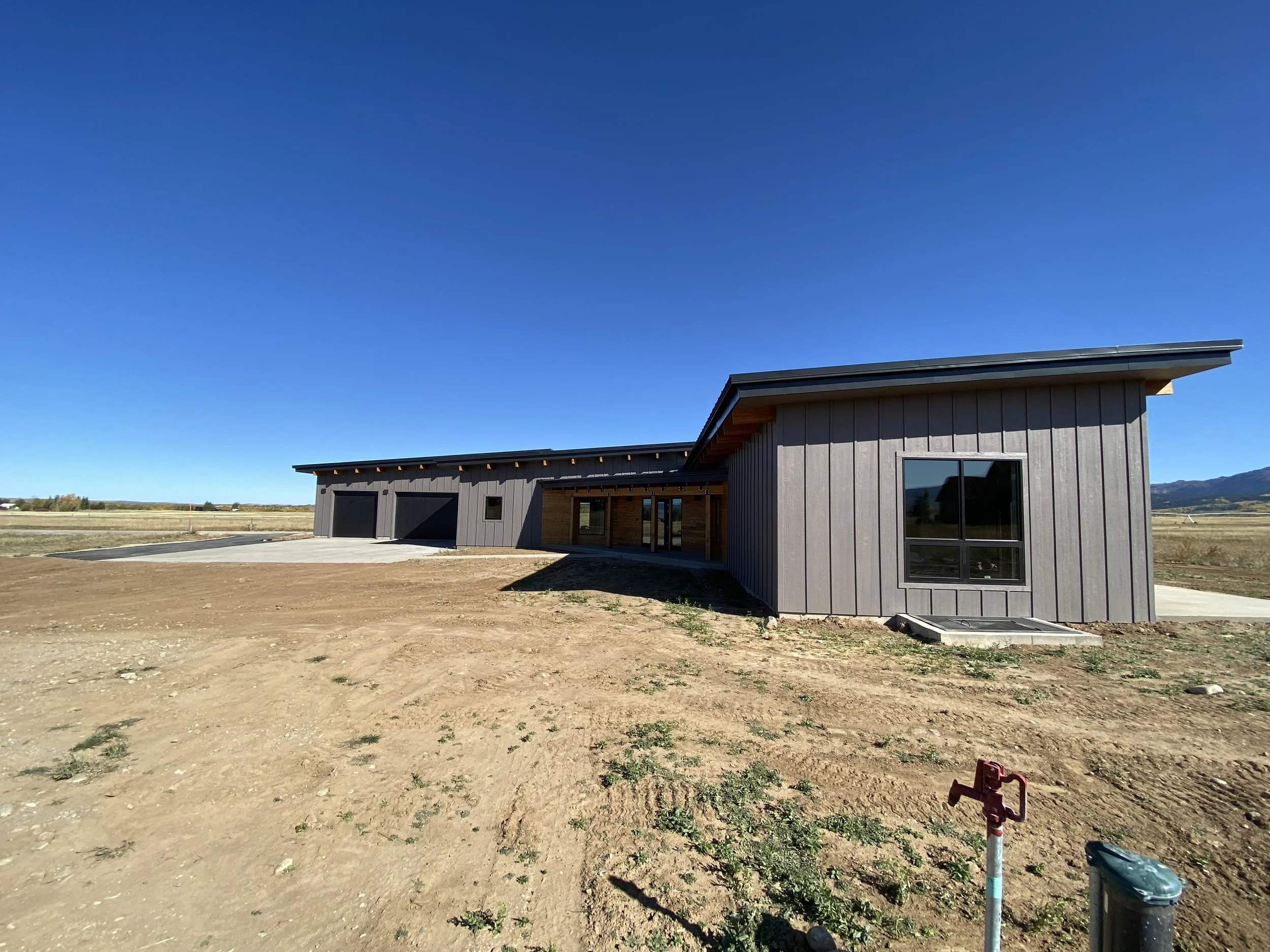 Custom home on acreage in Eastern Idaho with expansive views and modern farmhouse design.
Newly constructed modern house with gray exterior, large windows, and a wooden entry area, set in a rural area with clear blue sky and mountains in Driggs, Idah
