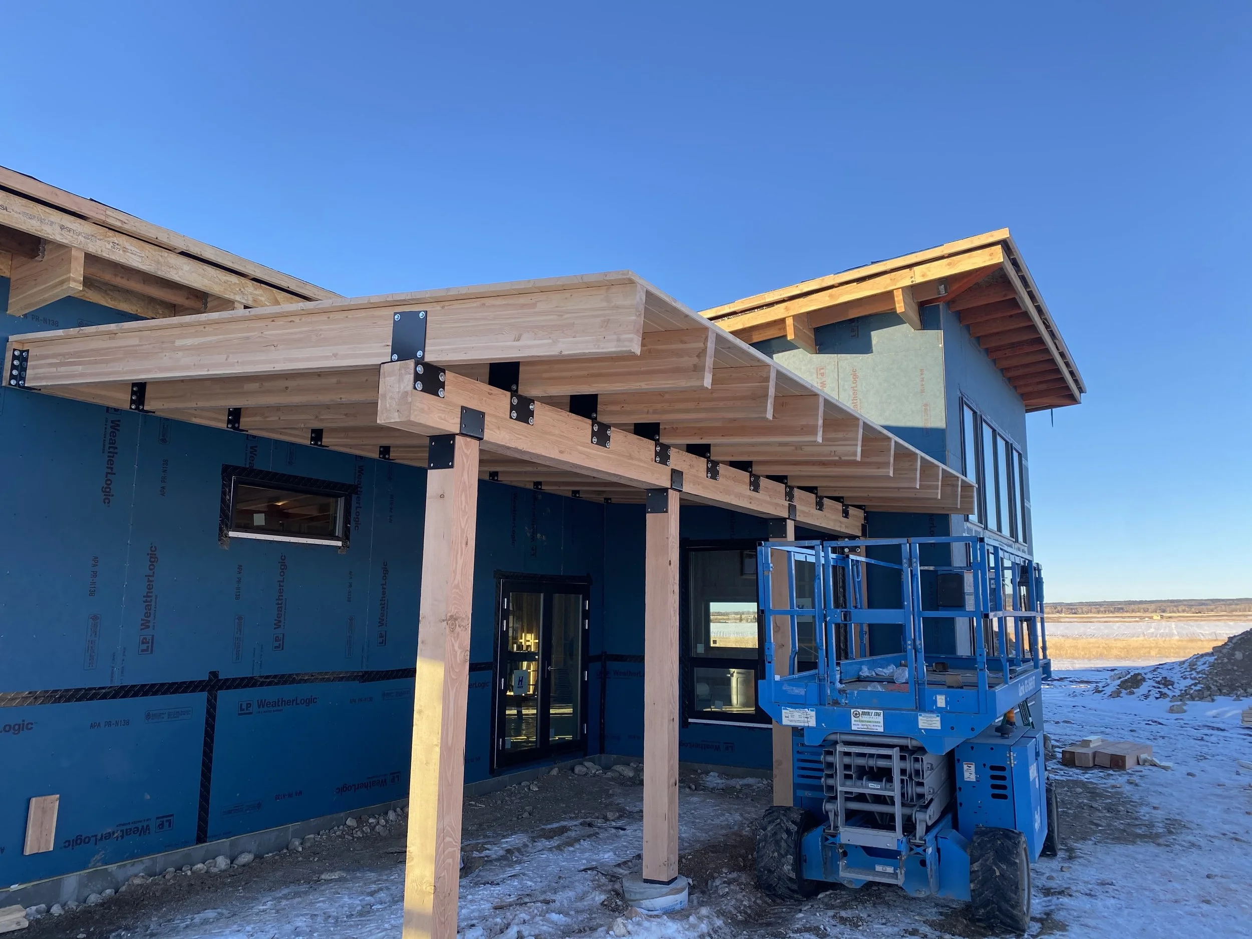 Under construction house with wooden framing, a blue lift, and a clear sky.