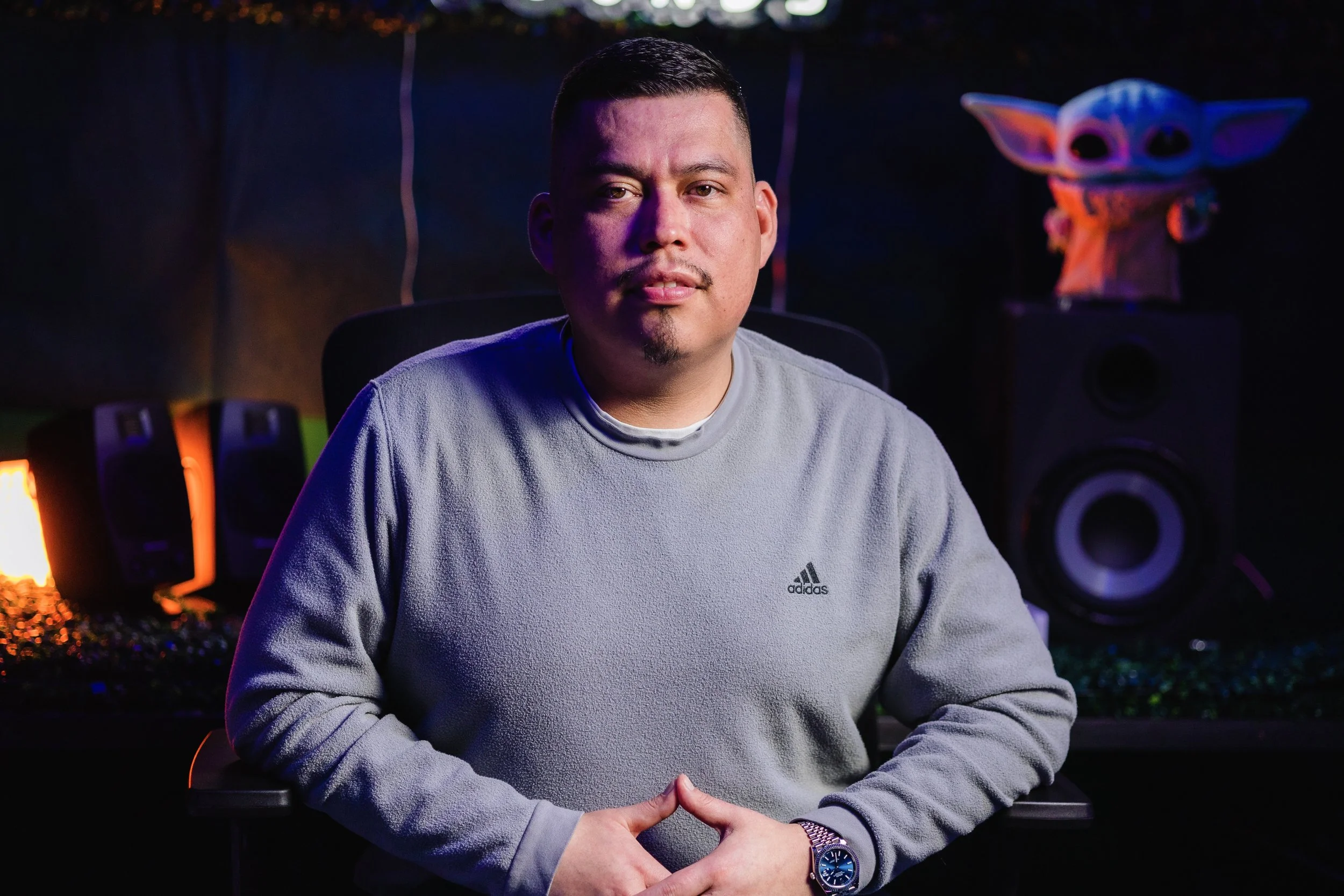 A man sitting in a recording studio with audio equipment and a Baby Yoda mask in the background.