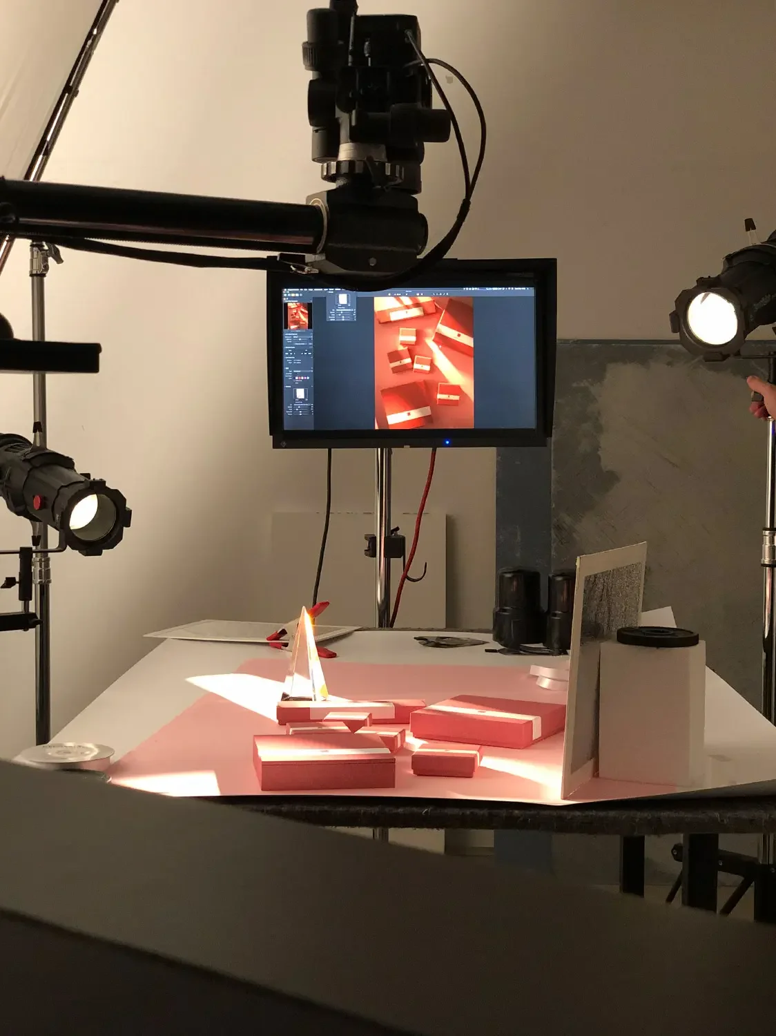 Photography setup with a camera, lighting, and a monitor displaying an image of red and white rectangular objects on a white table.