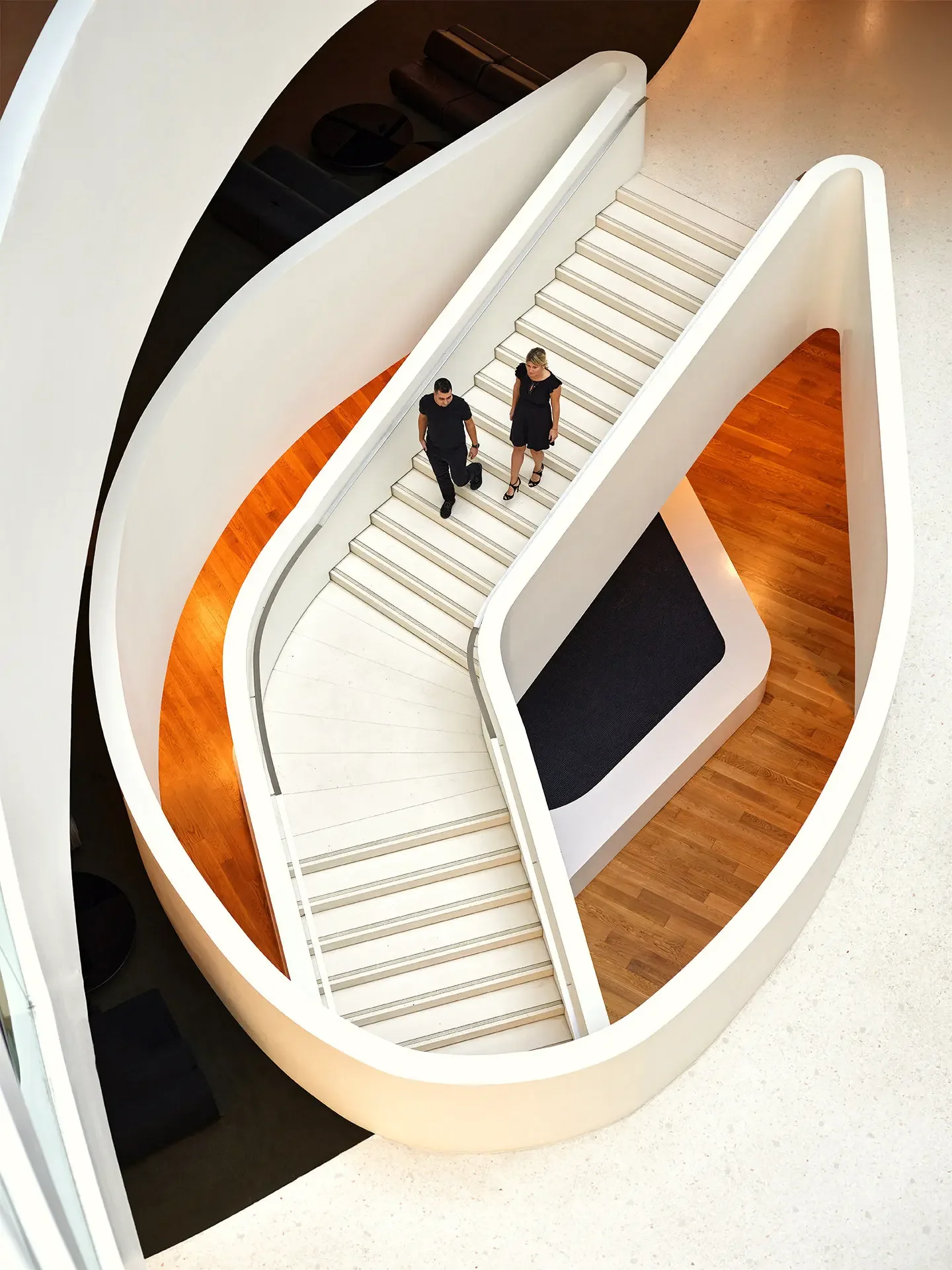 Two people walking down a white, modern staircase in a contemporary building with wooden and white accents.