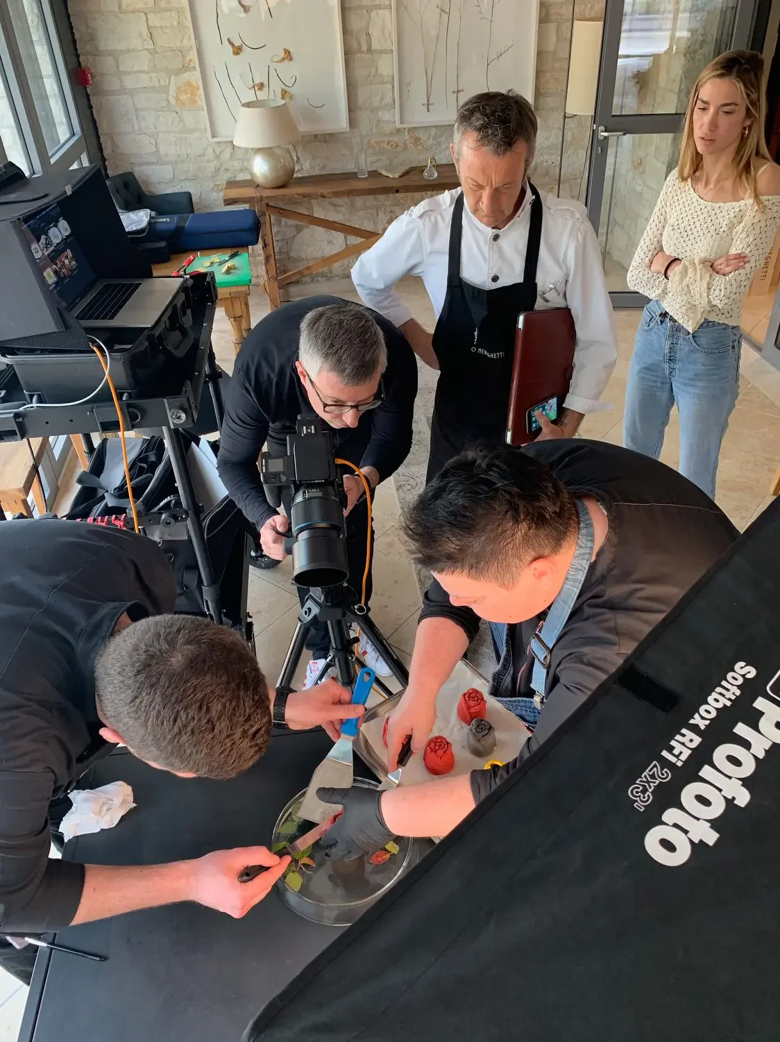 Group of people, including a chef, filming a culinary demonstration with various colorful ingredients and kitchen tools on a table.