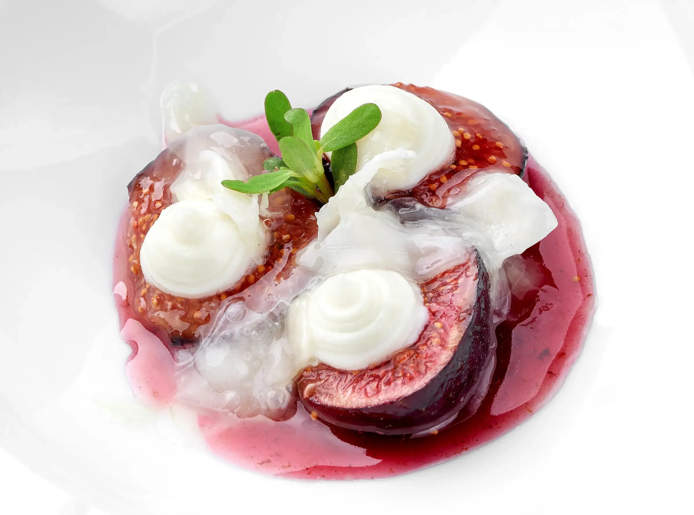 Close-up of a dessert with fresh figs, whipped cream, and a sprig of green herbs on a white plate.
