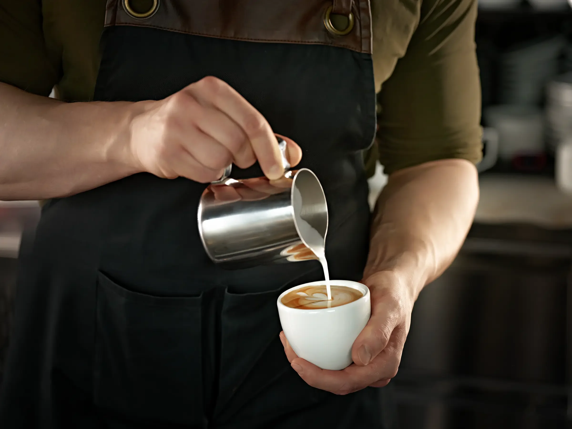 Barista pouring steamed milk into a cup of espresso to make latte art.