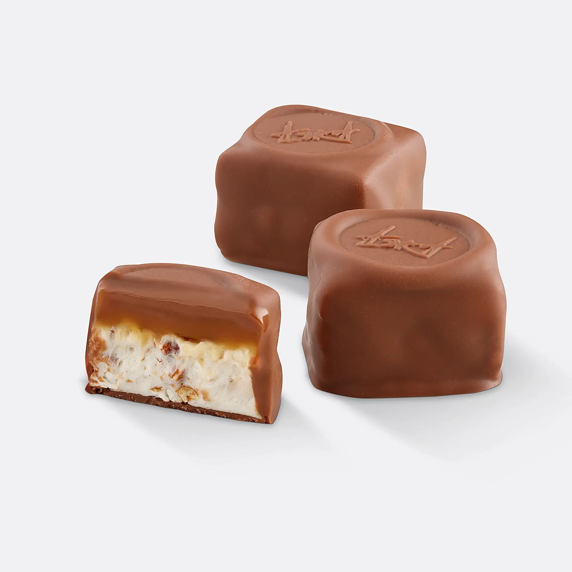 Three square chocolates with smooth milk chocolate coating, one broken to reveal caramel and nougat filling inside.