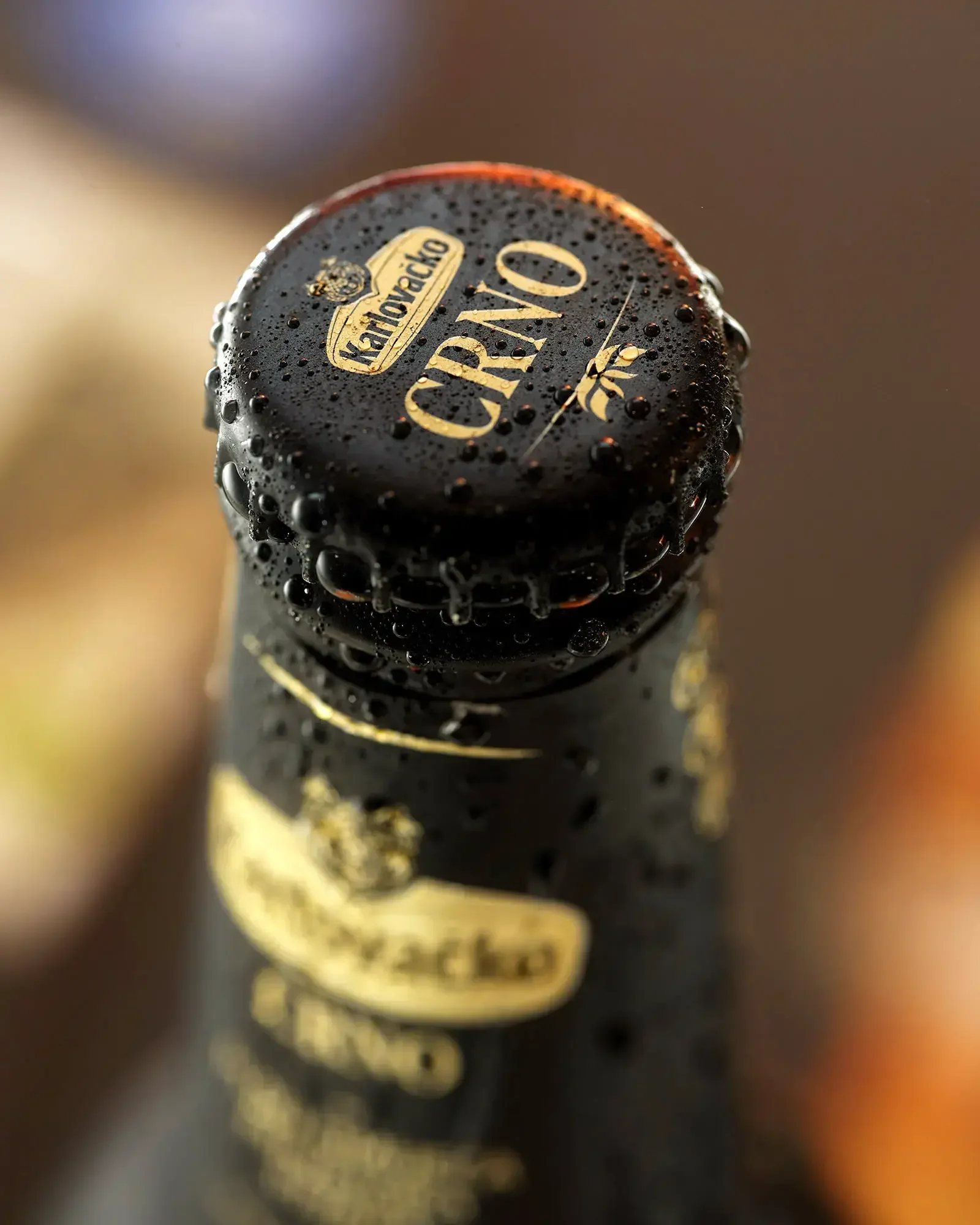 Close-up of the top of a dark beer bottle with condensation, showing the cap with gold lettering that reads 'Karlovacko' and 'CRVO', along with decorative elements.