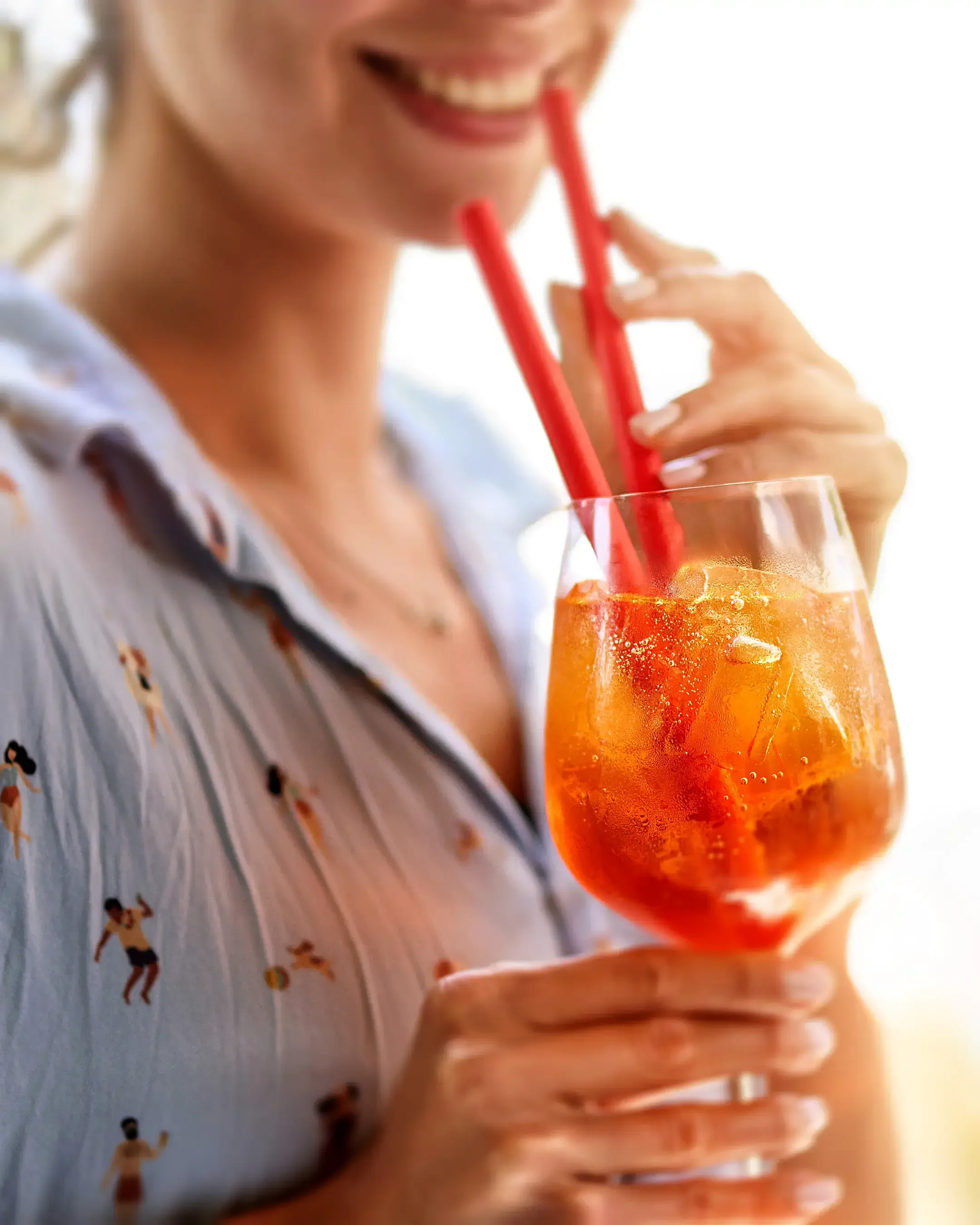 A woman smiling and drinking a large glass of orange-colored beverage through two red straws.