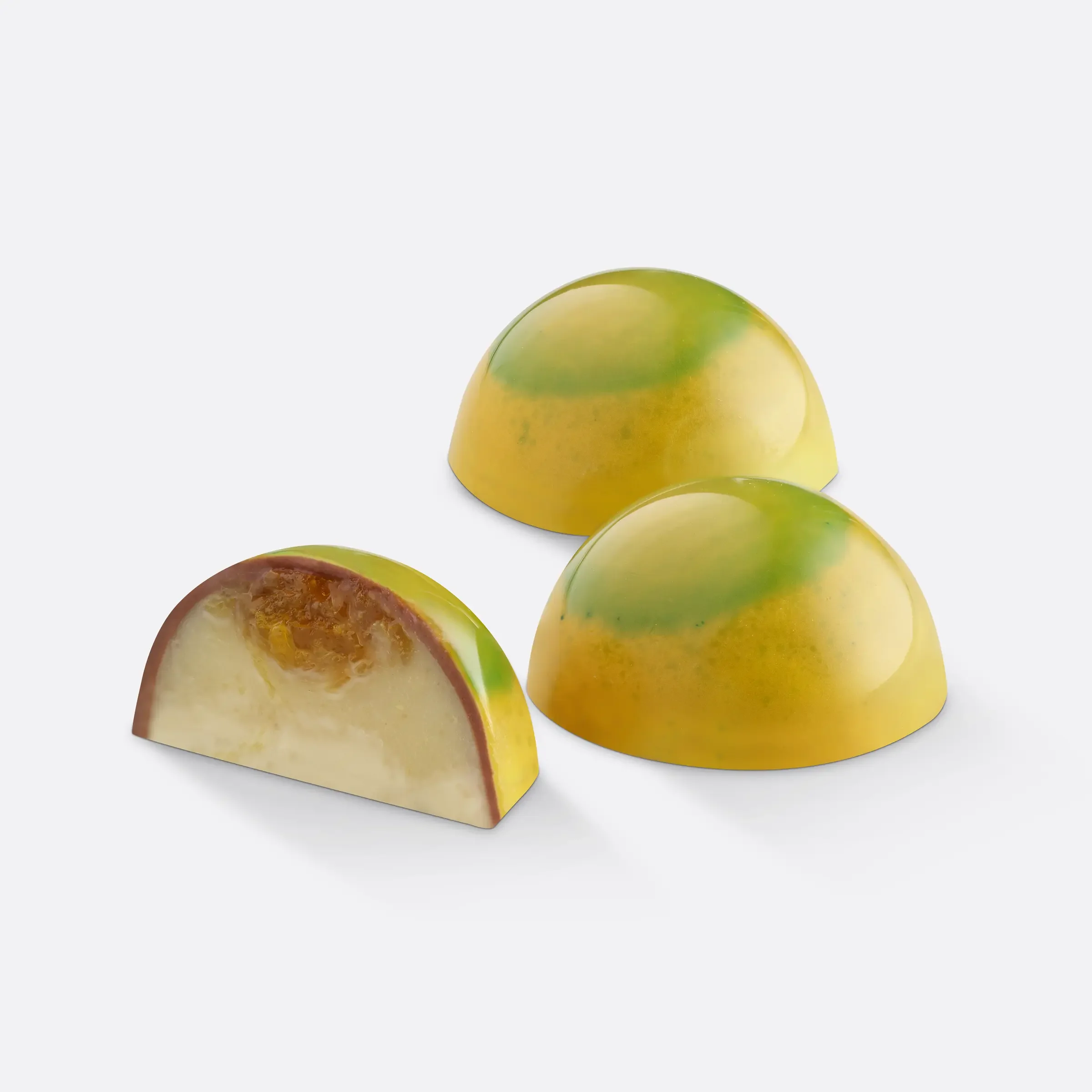 Three yellow and green chocolate truffles with one cut open to show a creamy filling.