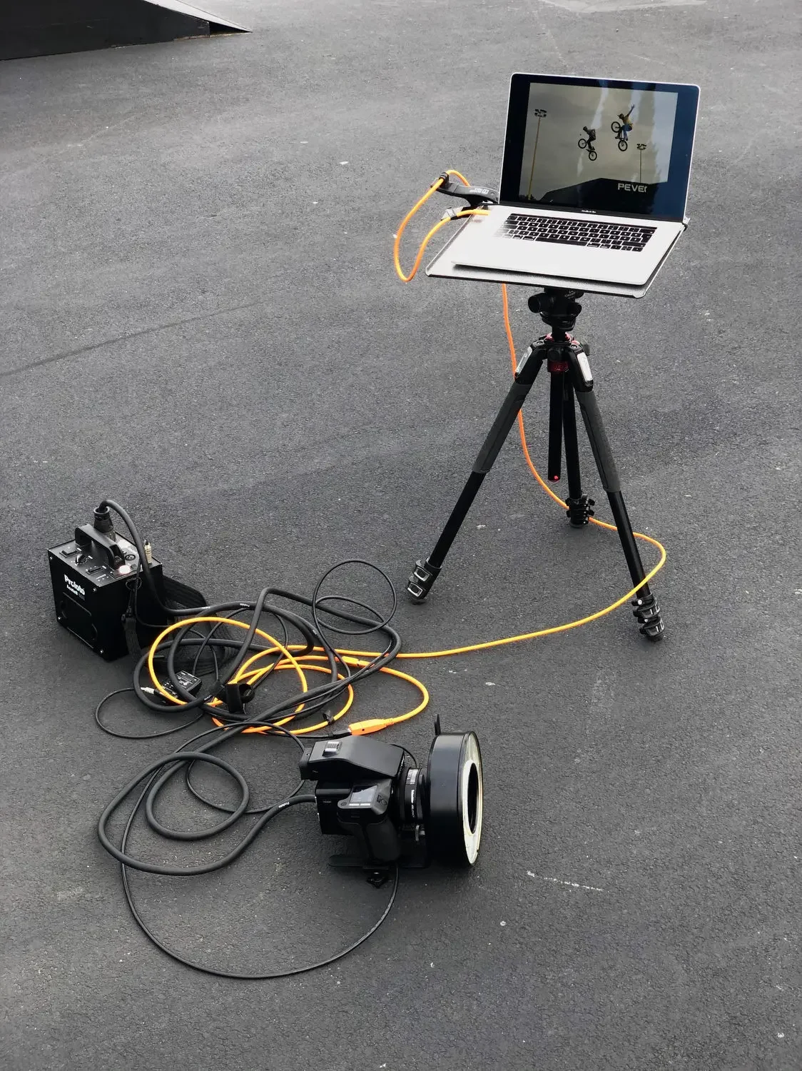 A camera setup with a laptop on a tripod, connected to a projector or specialized camera equipment, displaying an image of two BMX bikers performing tricks.