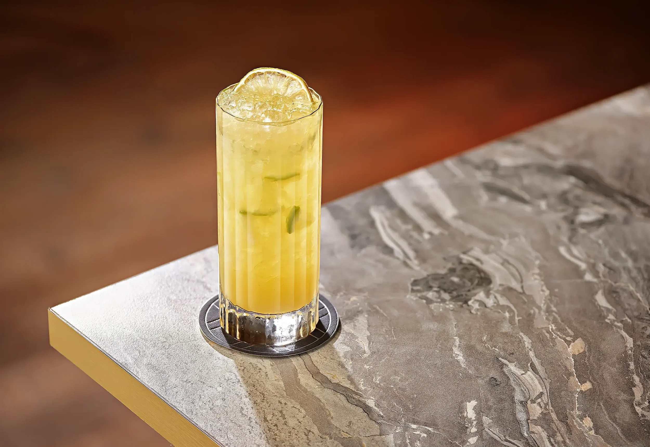 A tall glass of lemonade with ice and lemon slices on a marble table.