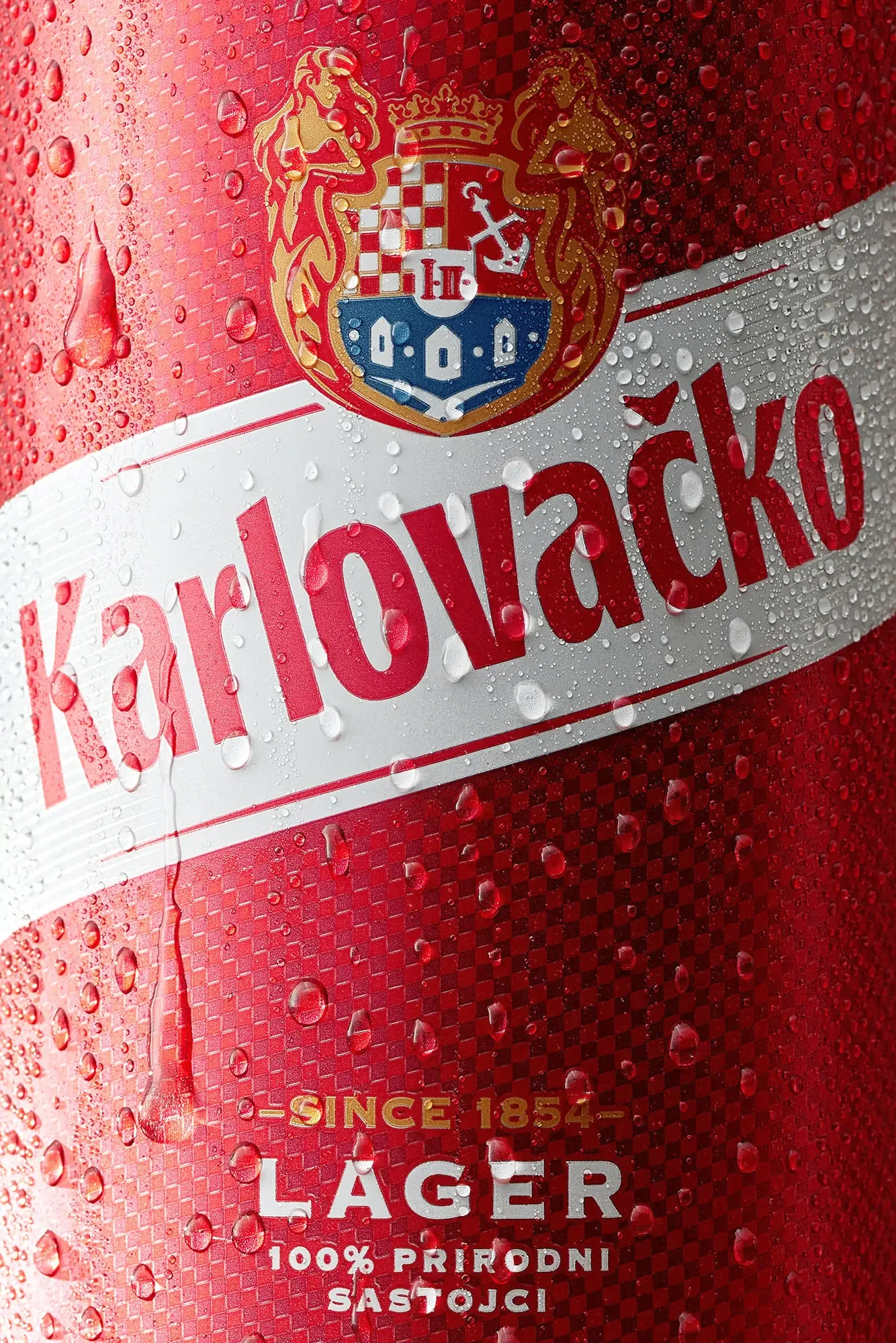 Close-up of a Karlovacko Lager beer can with water droplets on its red and silver surface.