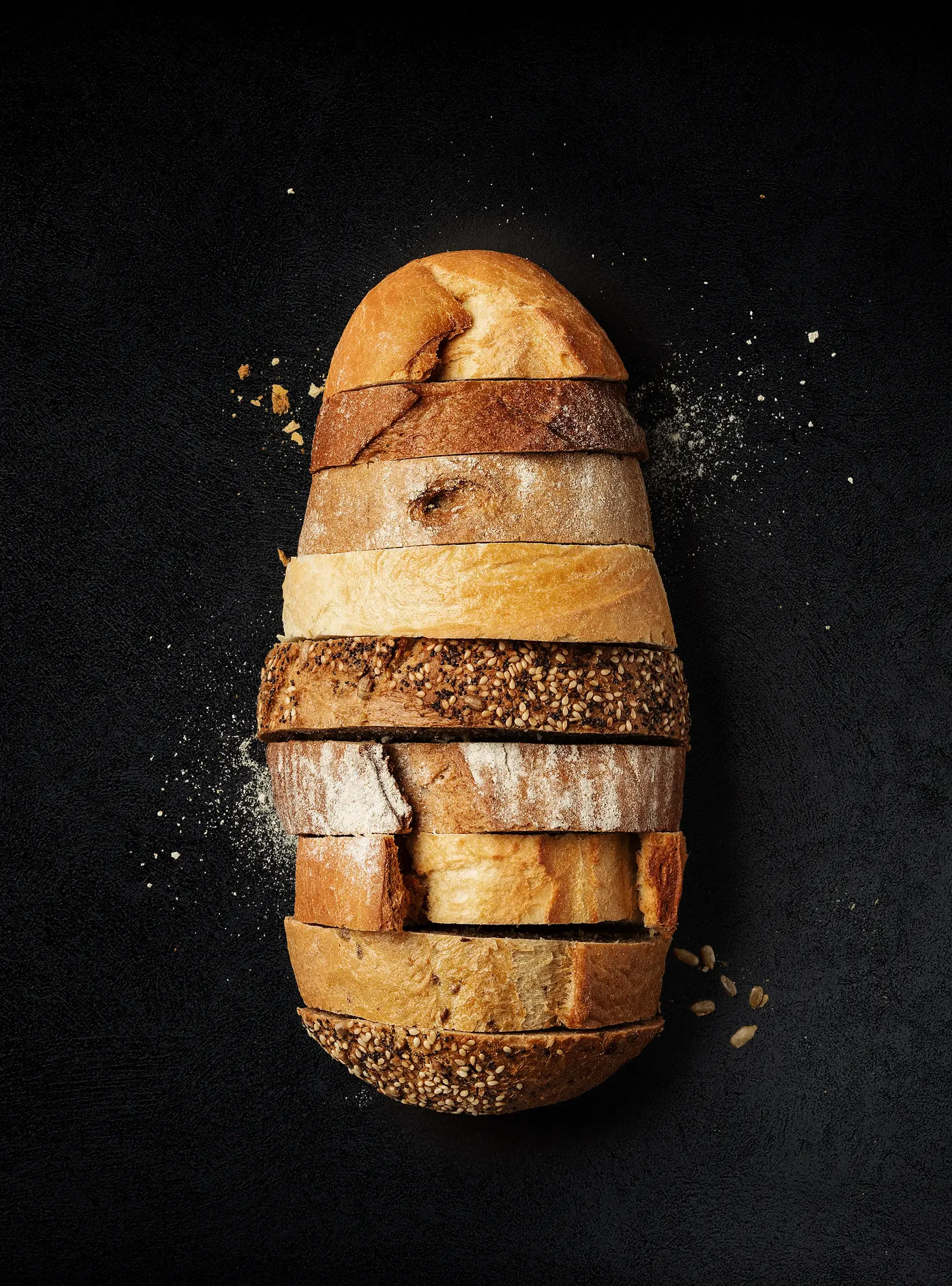 Assorted slices of bread arranged vertically on a black background with some flour and crumbs scattered around.