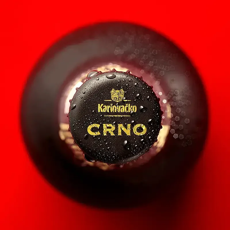 Top view of a dark beer bottle with a glistening black cap featuring the Karlo Vačko logo and the text 'ČRNO' against a red background.