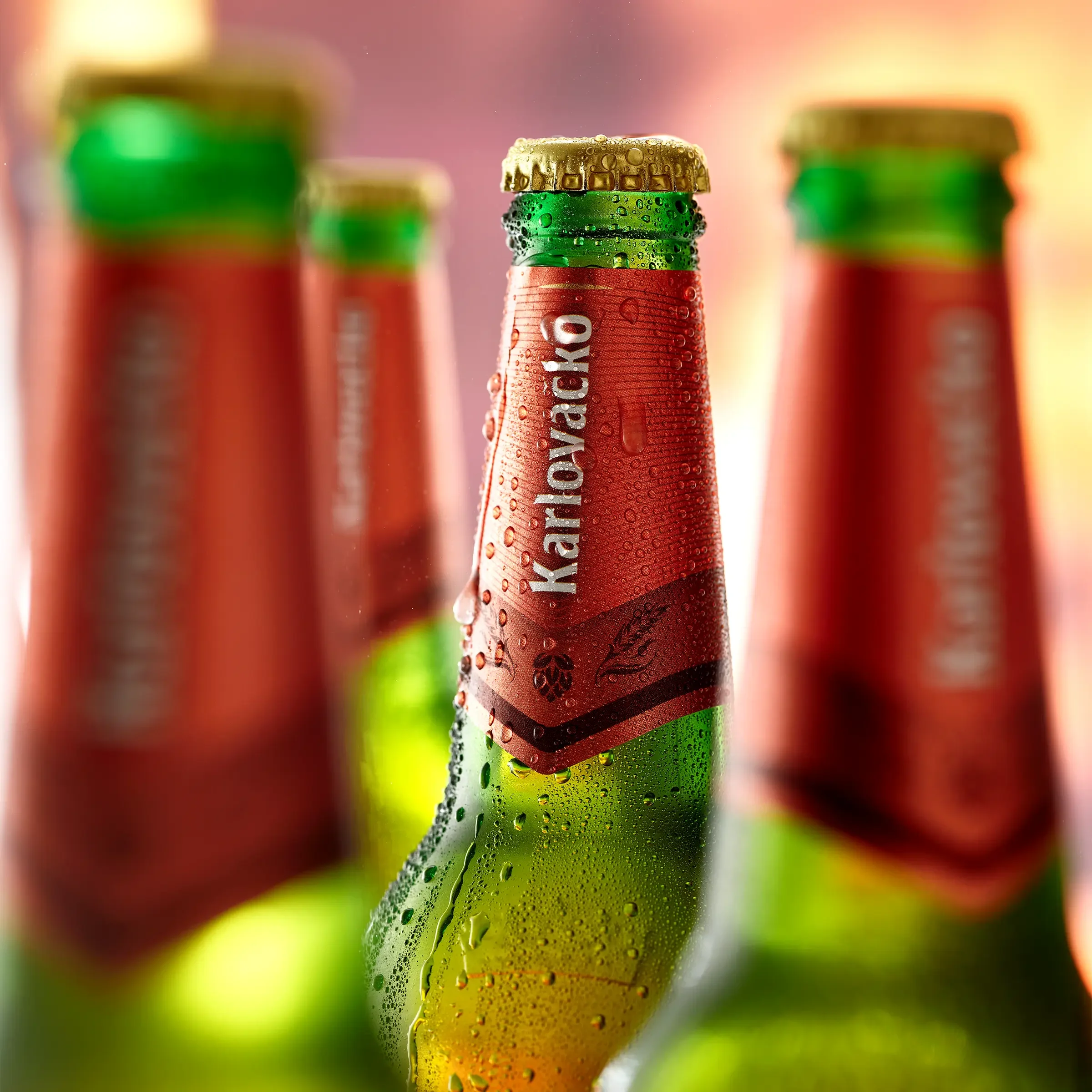 Close-up of a green bottled beverage with condensation and a red label, with other similar bottles blurred in the background.