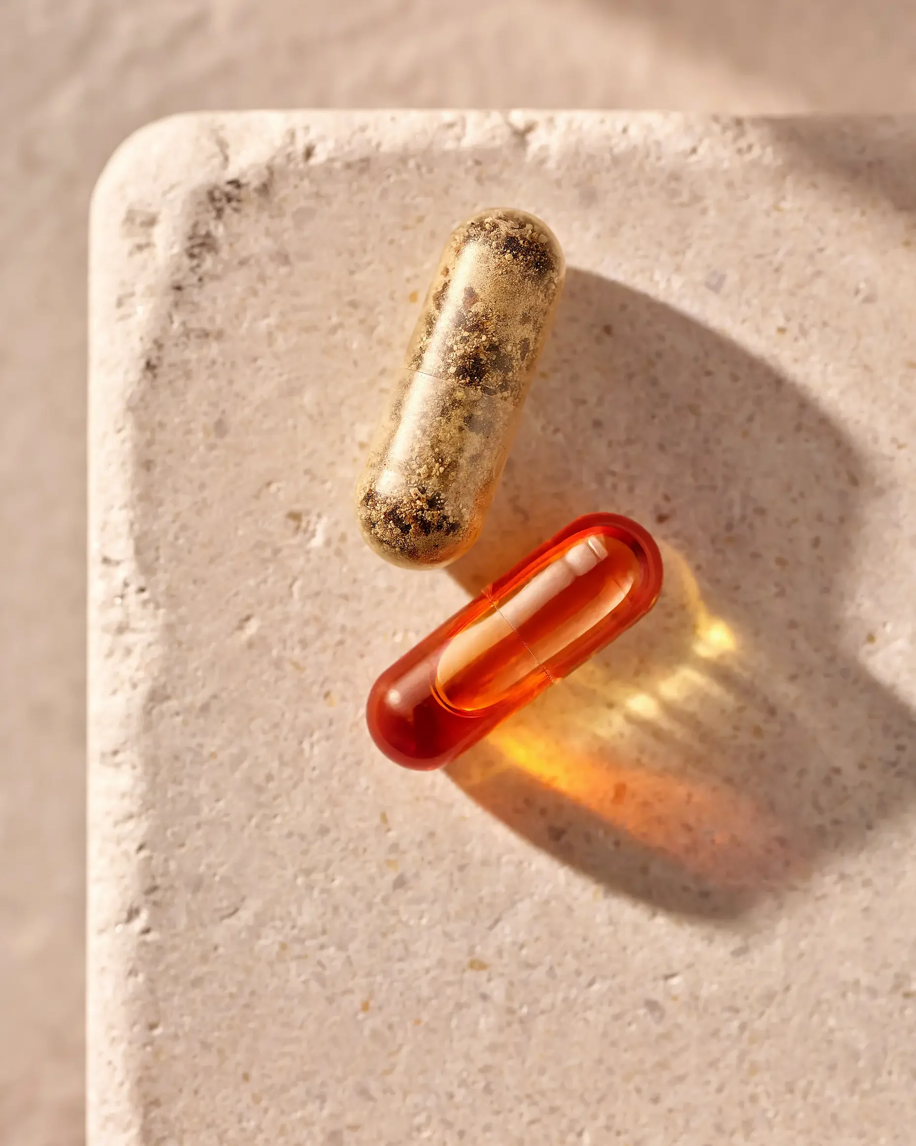 A stone surface with a transparent red capsule-shaped pill and a dirty capsule-shaped pill with a mottled appearance placed on top.