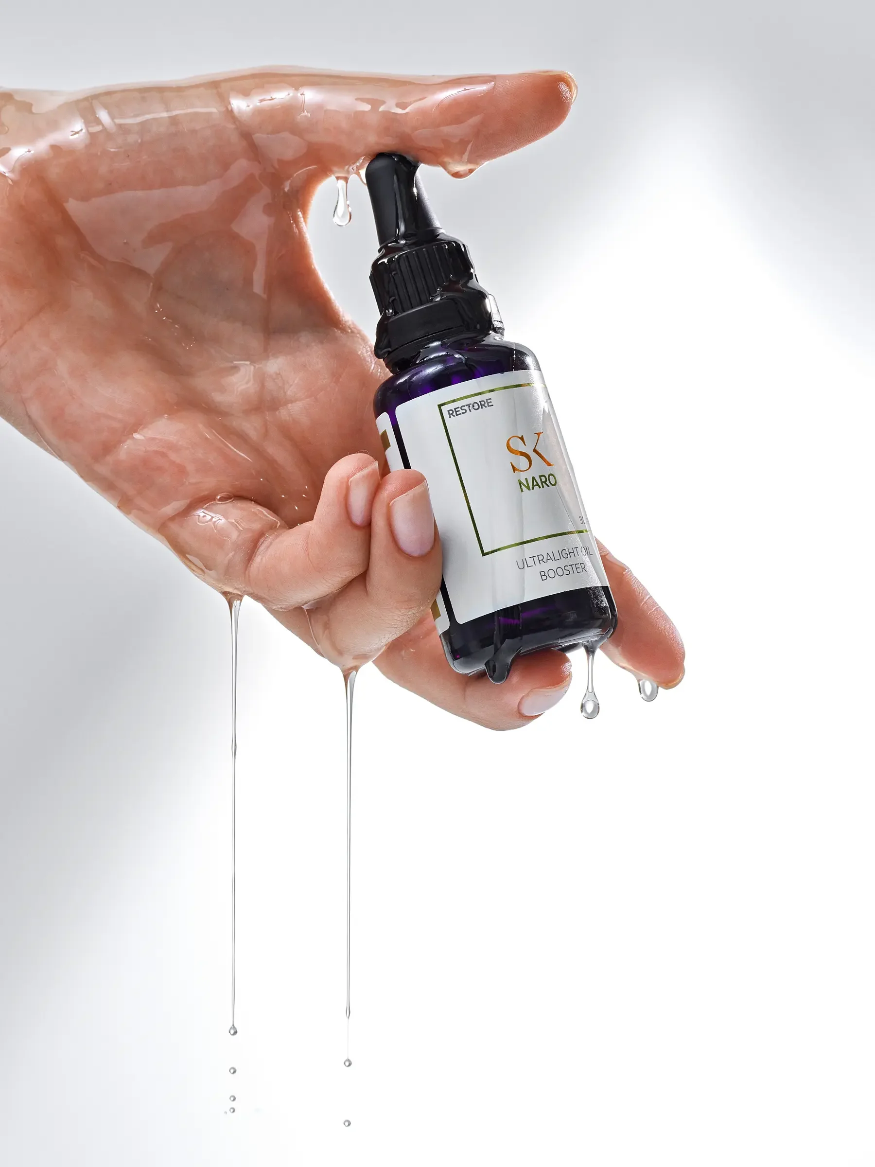 A hand holding a small dark purple bottle labeled 'SK NARO' with a dropper cap, with liquid dripping from the dropper and the bottle.