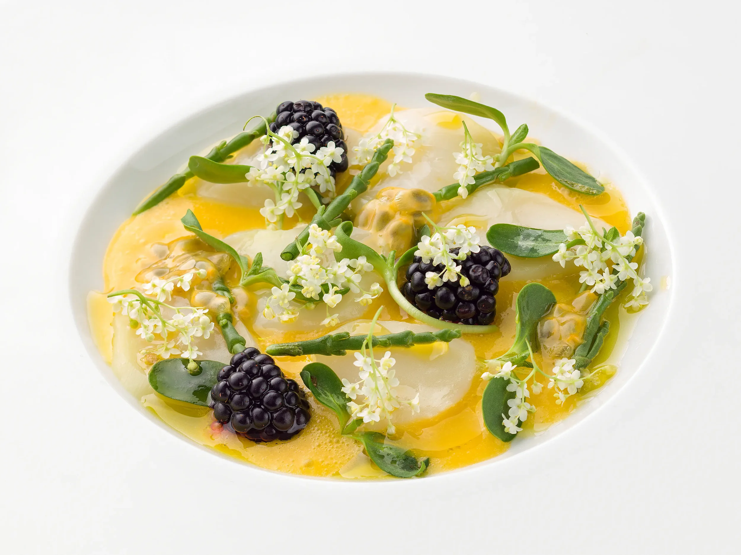 Salad with blackberries, edible flowers, green herbs, and a yellow dressing